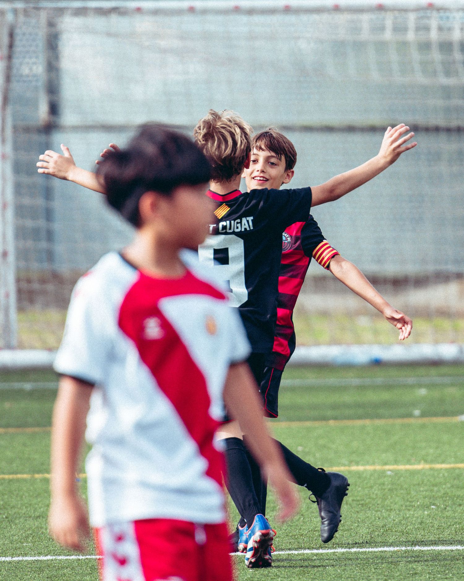 Two youth soccer players celebrate with a hug during a match on a green field.