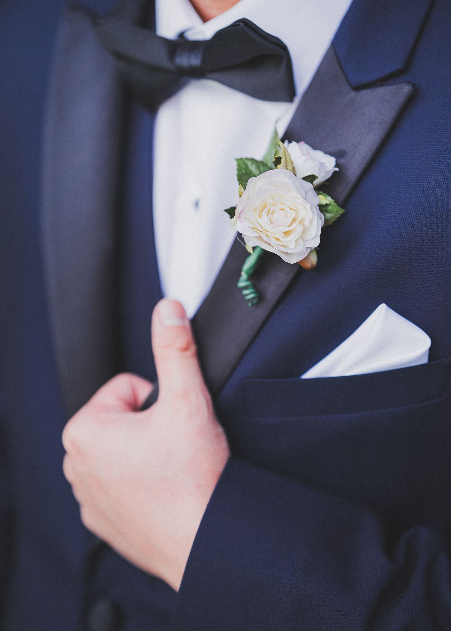 Detail shots of a white rose boutonniere pinned to a navy blue suit jacket.