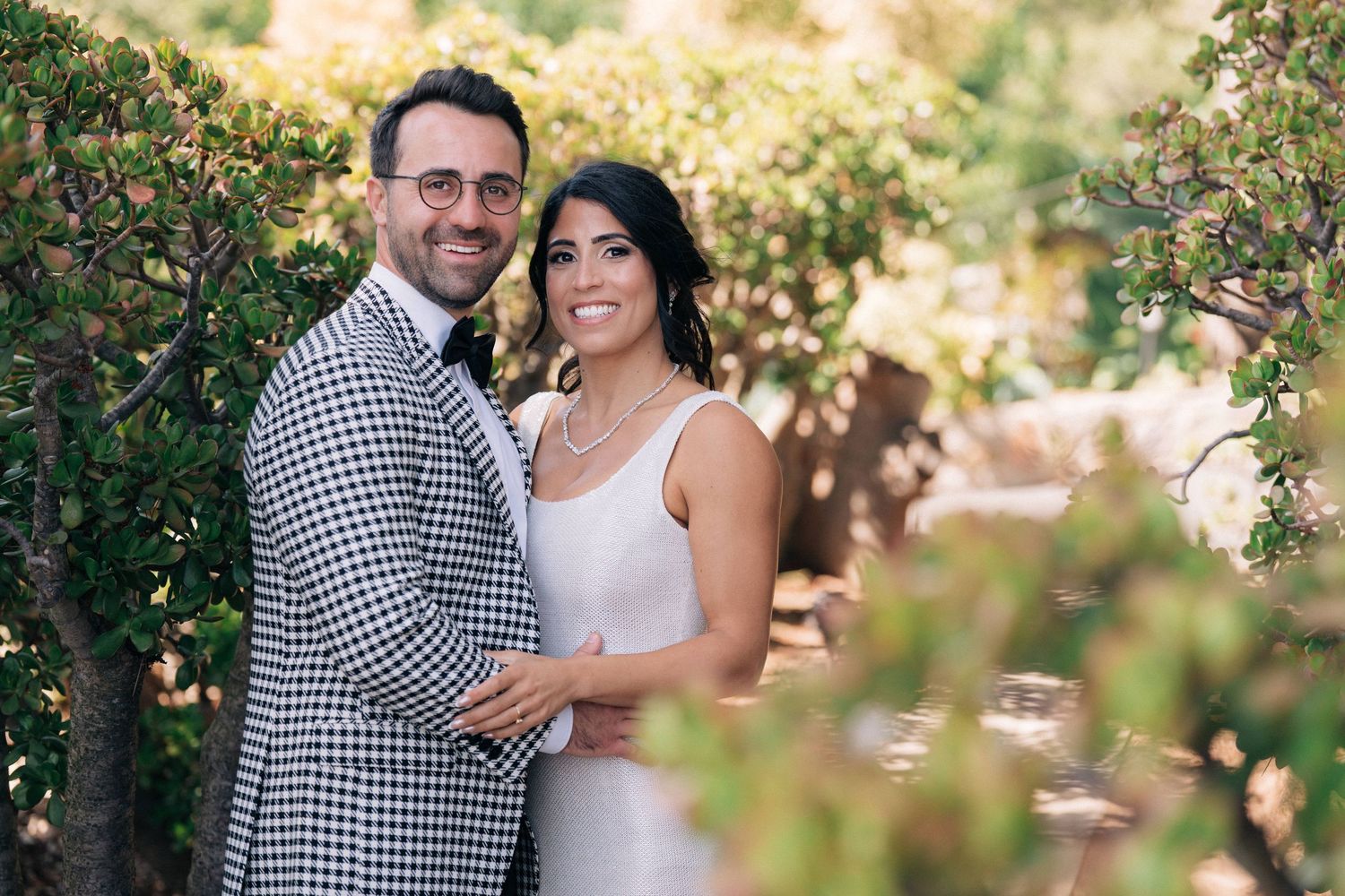 A romantic wedding photo of a couple embracing in a garden setting with soft natural lighting and floral elements.