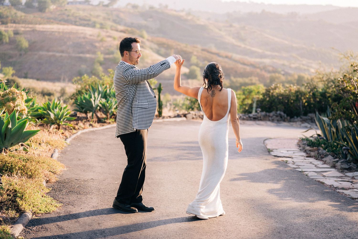 A playful moment between newlyweds dancing on a scenic hilltop path during golden hour.