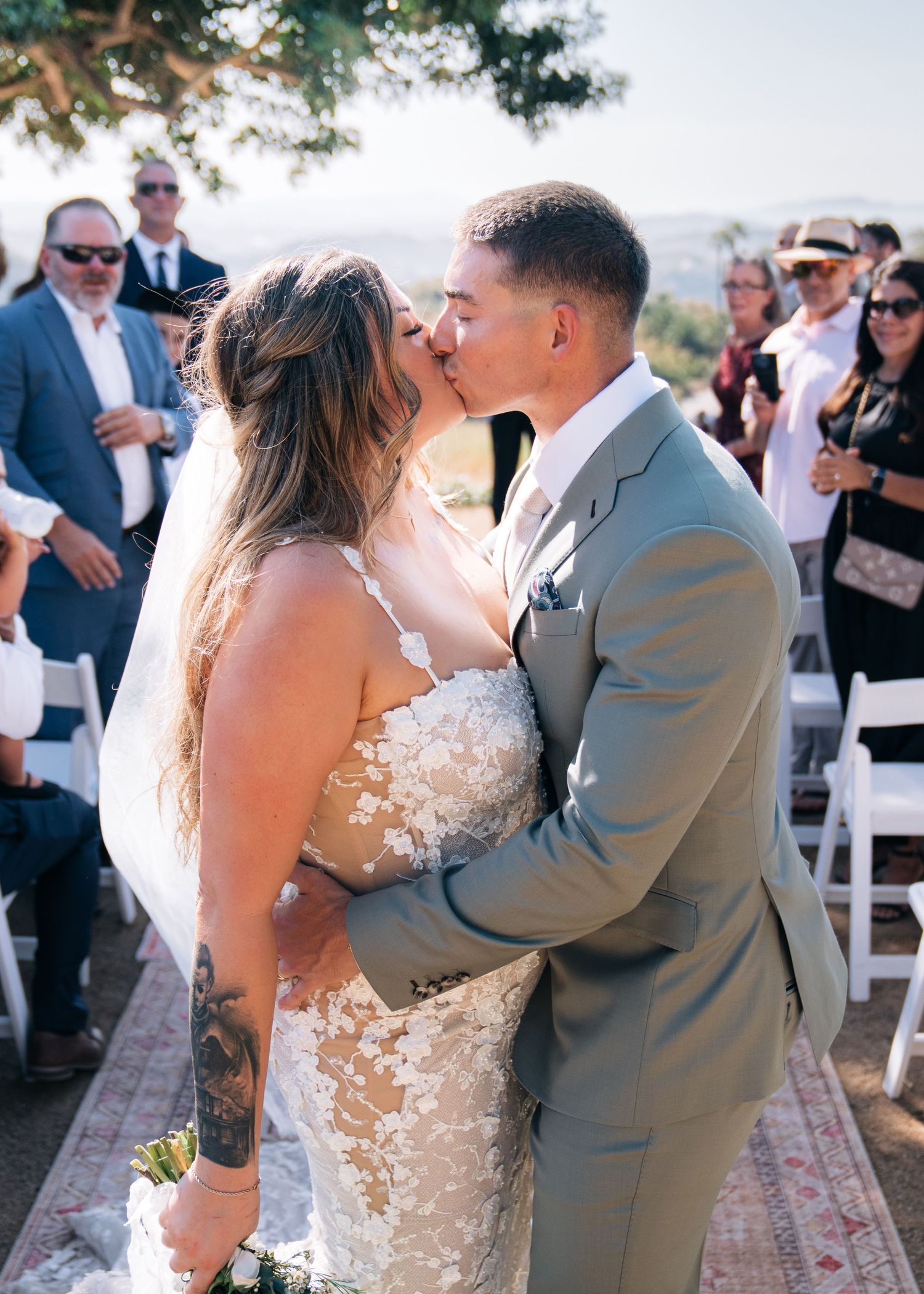 Four romantic photos of a couple sharing their first kiss as newlyweds during an outdoor wedding ceremony.