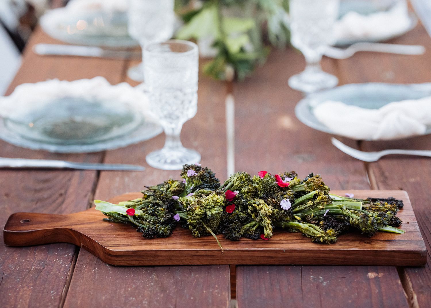 Fresh green salad served on wooden board with elegant table settings and crystal glassware.