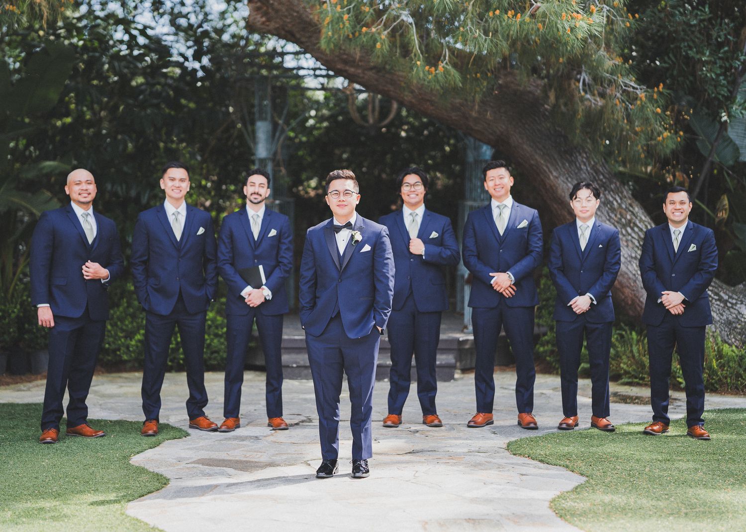 Groomsmen in matching navy suits posing outdoors for formal wedding photos.