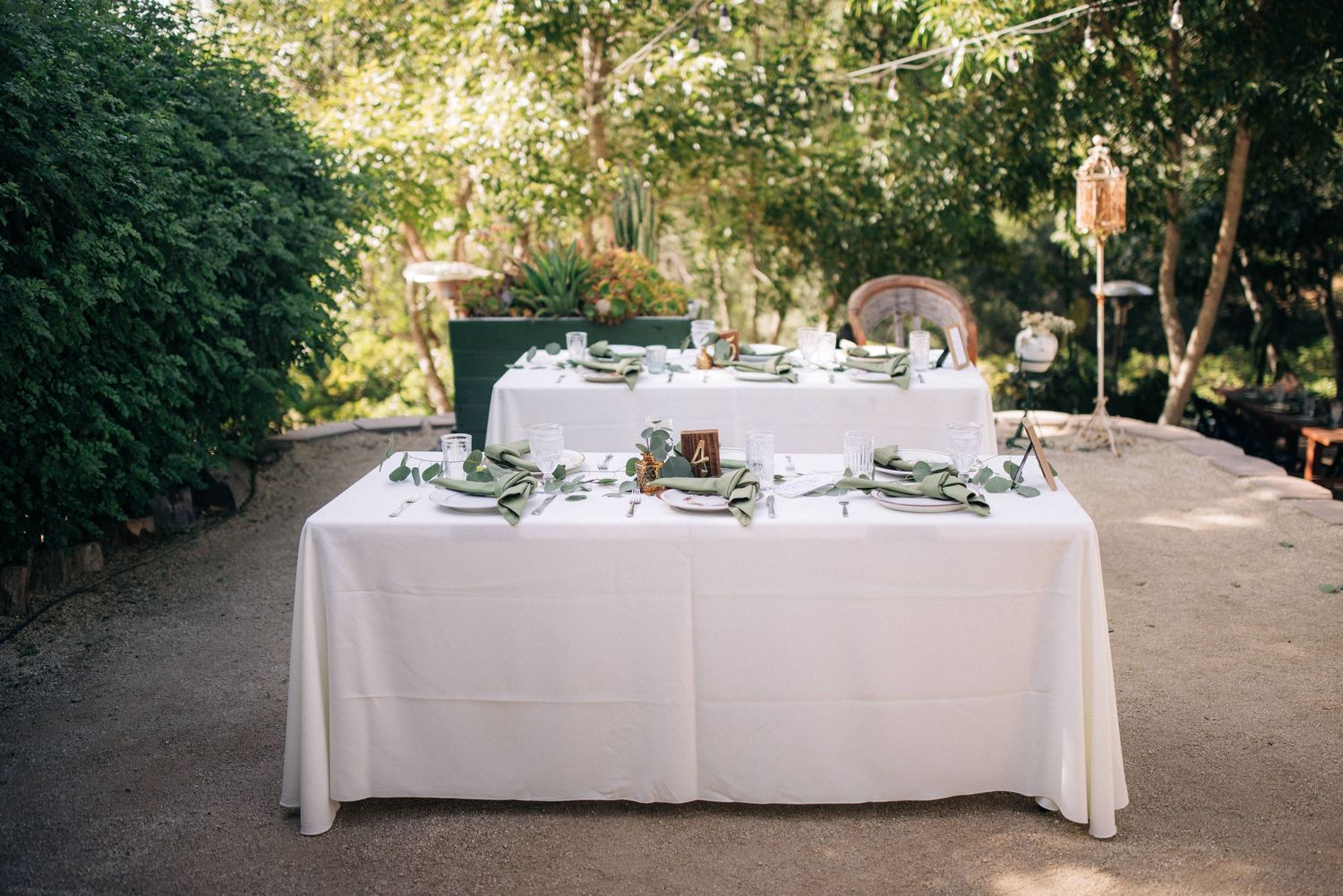 White tablecloth covered table set for dining with place settings in an outdoor garden venue.