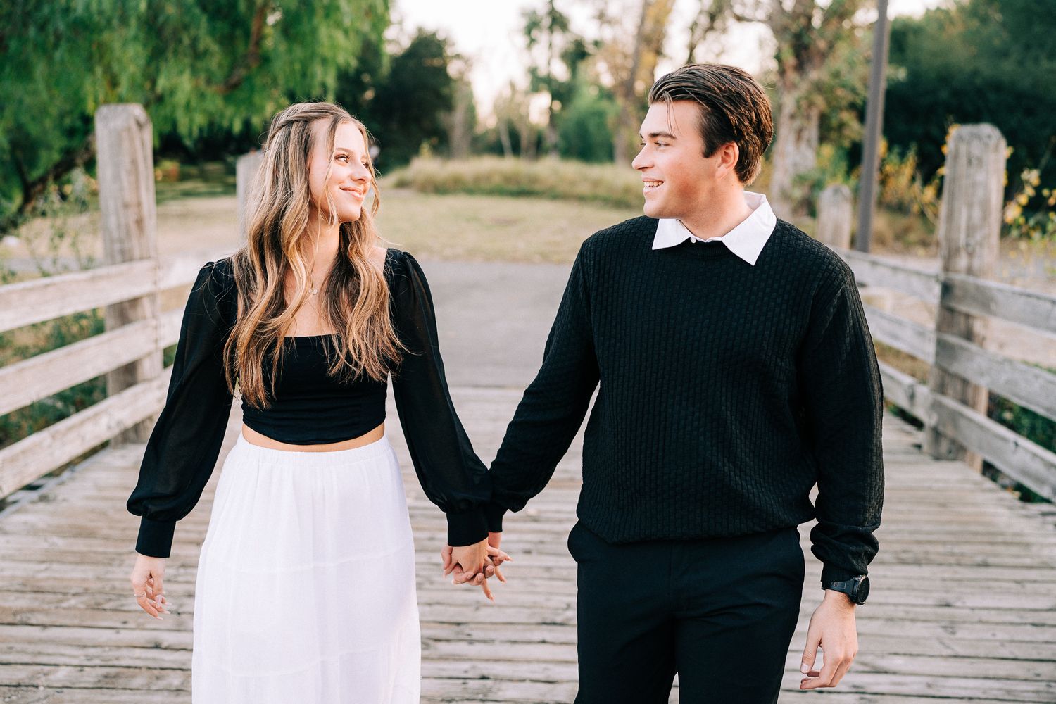 A couple holding hands while walking on a wooden bridge in matching black and white clothing.