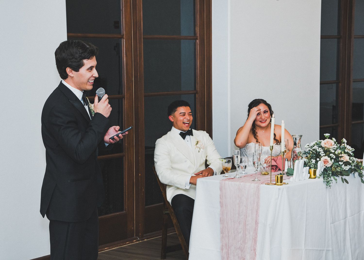 Wedding reception celebration capturing joyful candid moments at the head table during dinner and speeches.