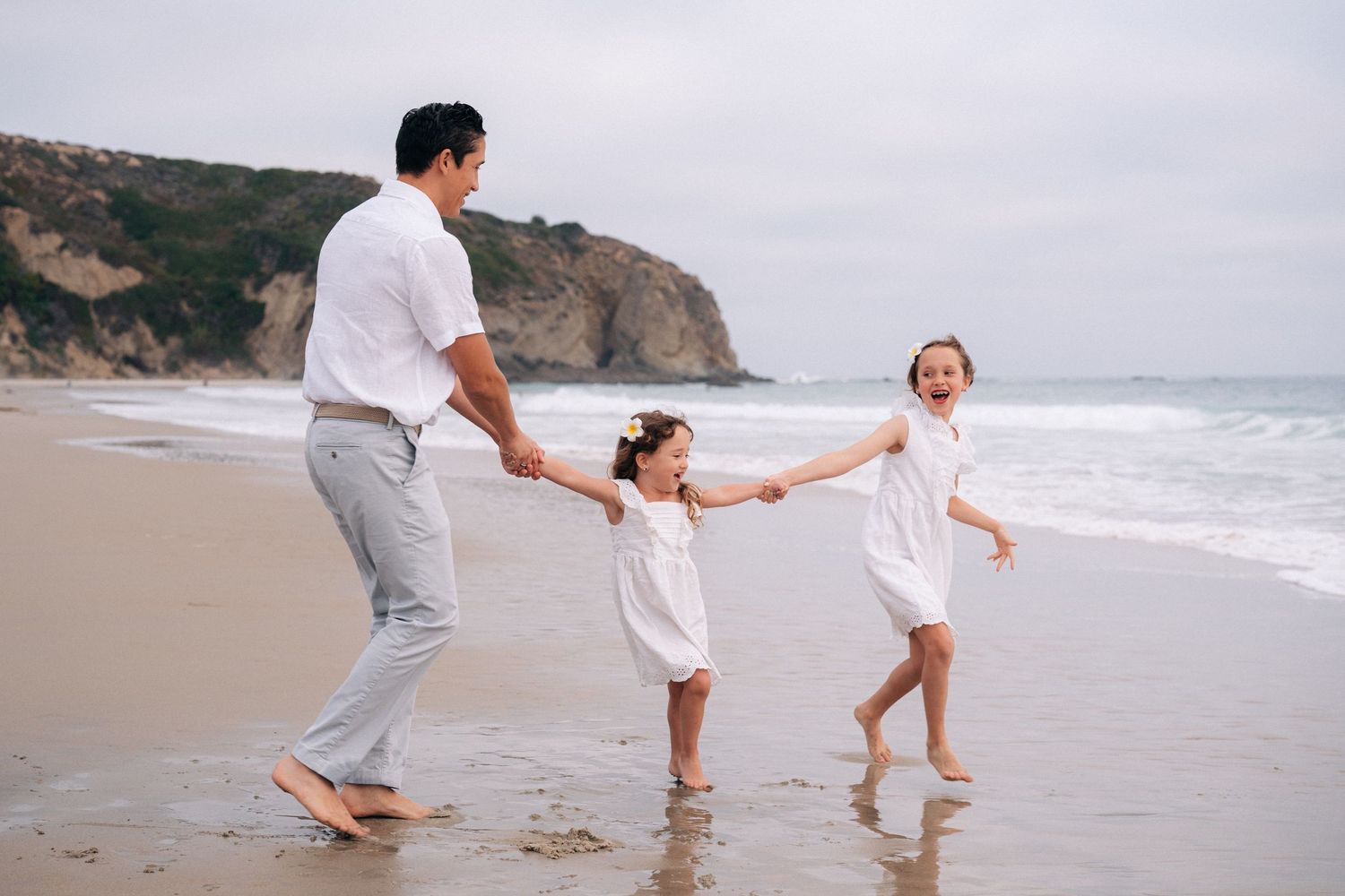 Family running and playing in the shallow ocean waves on an overcast beach day.