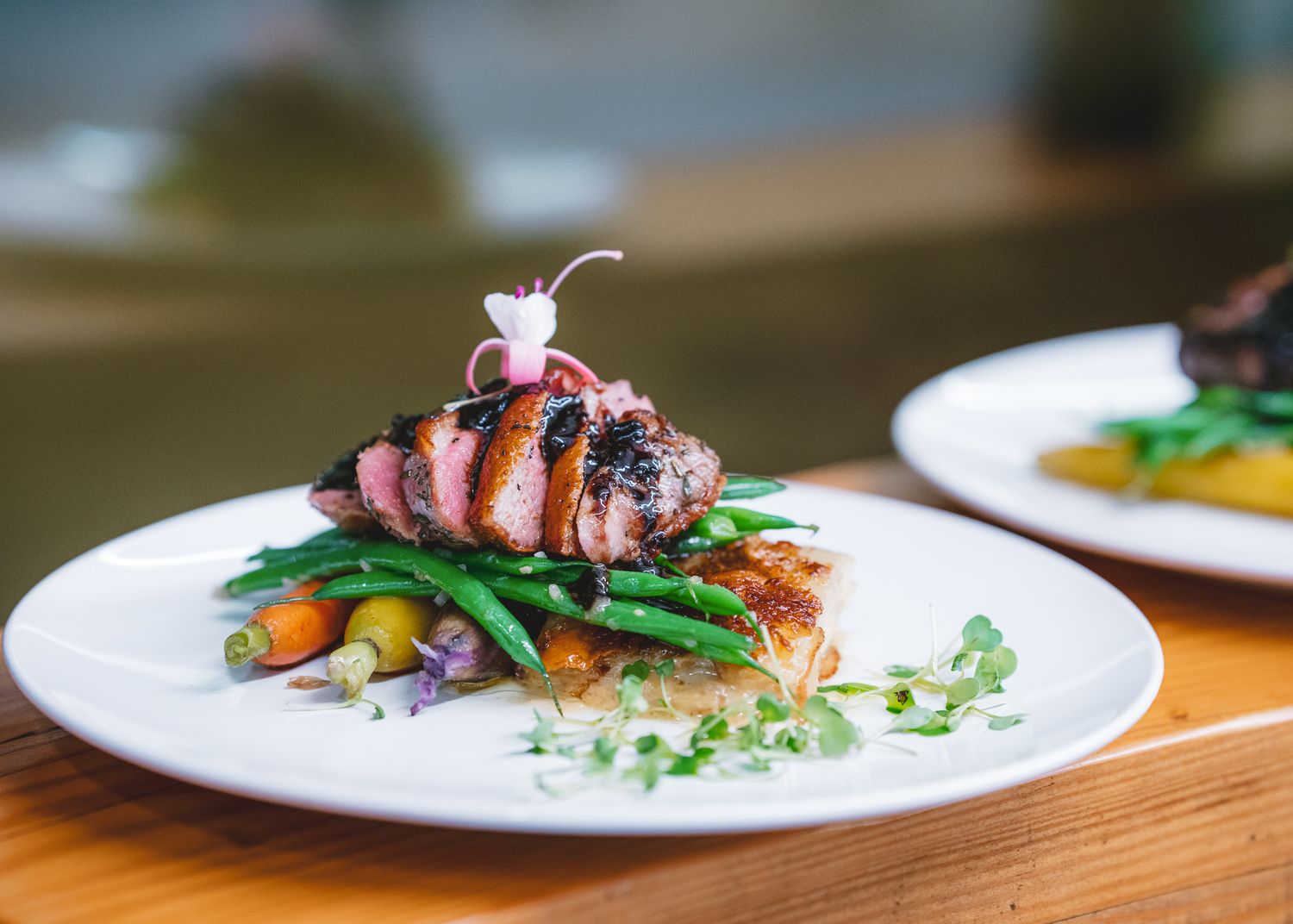 Grilled duck breast with cherry sauce served atop green beans and colorful vegetables on a pristine white plate.