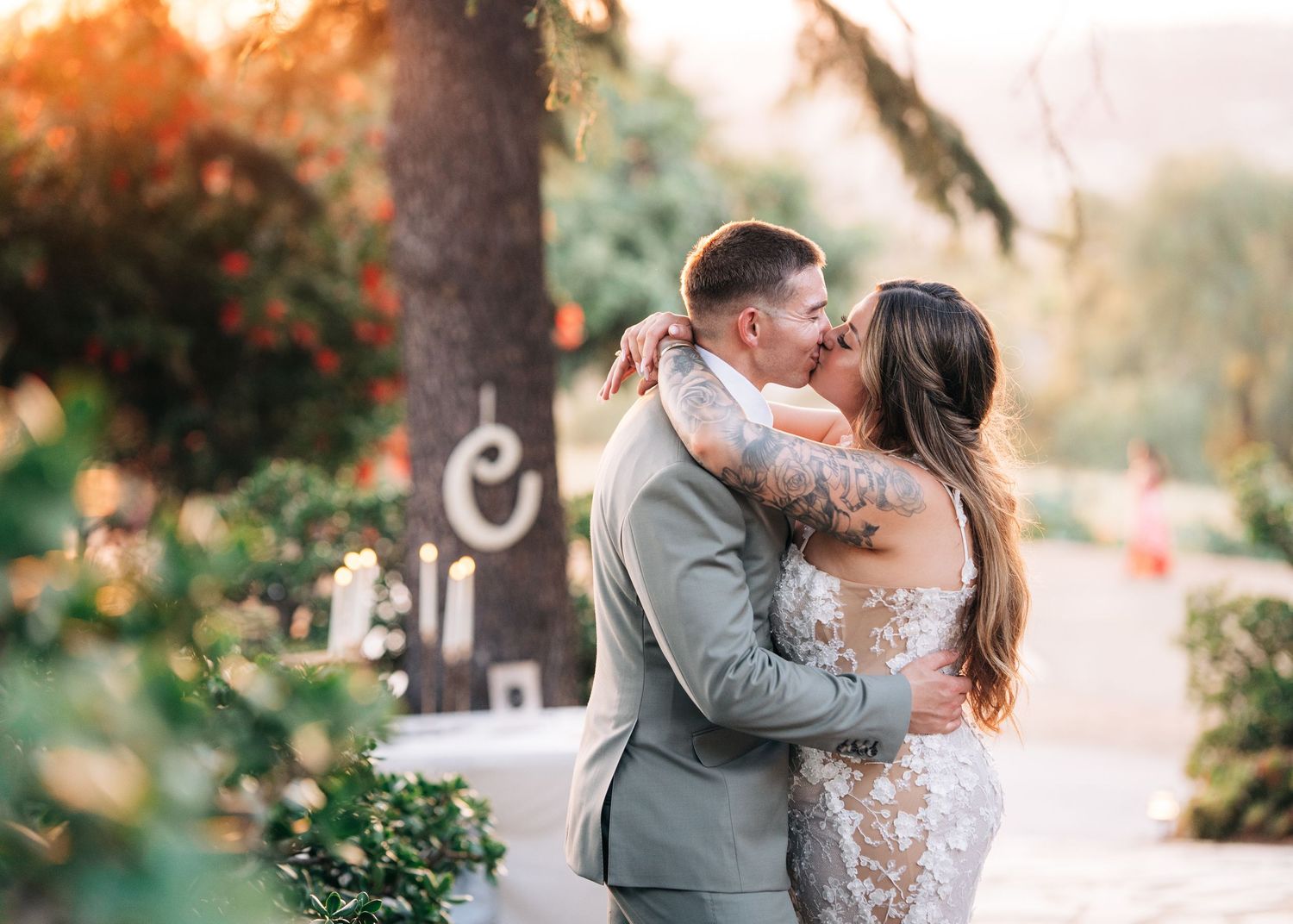 A couple in gray attire sharing an intimate moment in an outdoor garden setting during sunset.