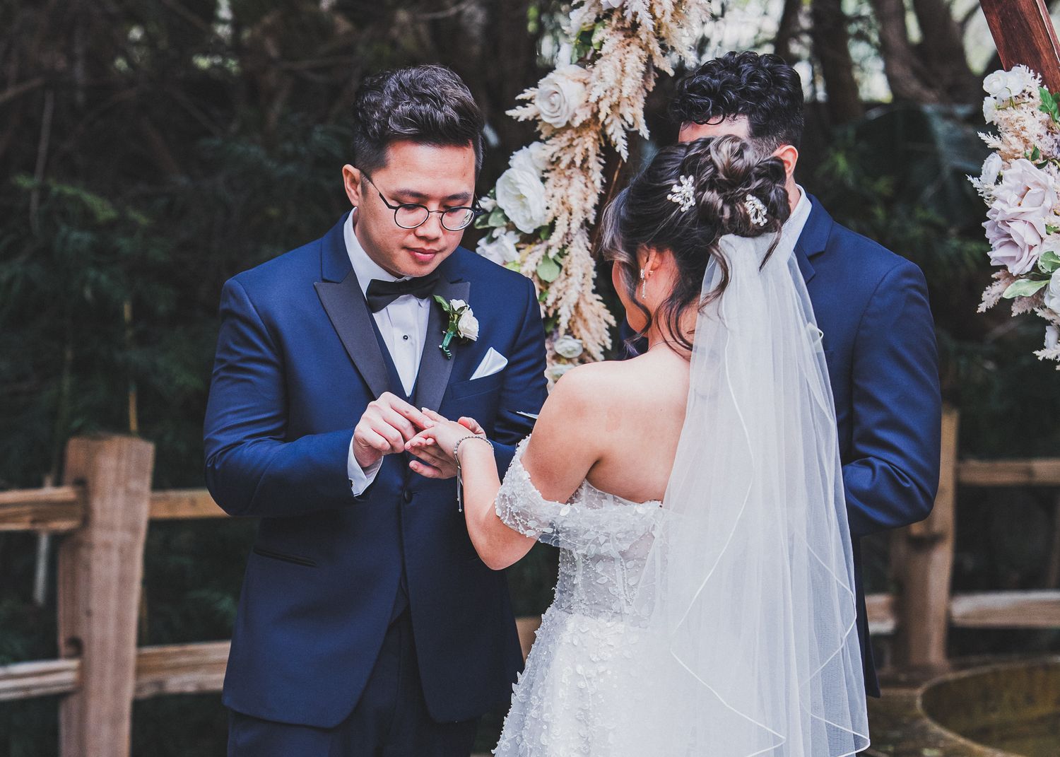 Couple exchanging rings during outdoor wedding ceremony with cherry blossoms.