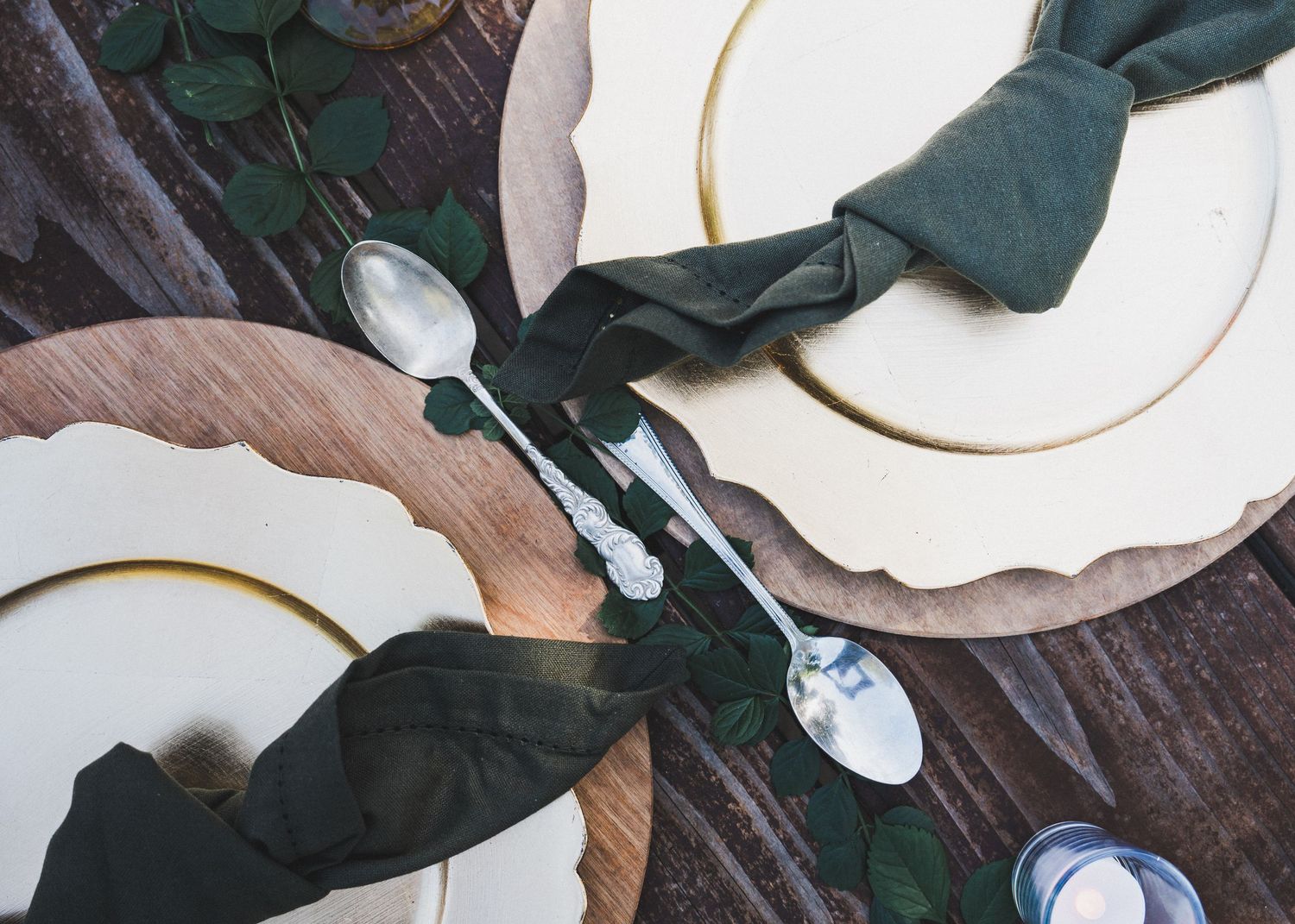 Rustic table setting with dark green napkins and white plates on wooden surface.