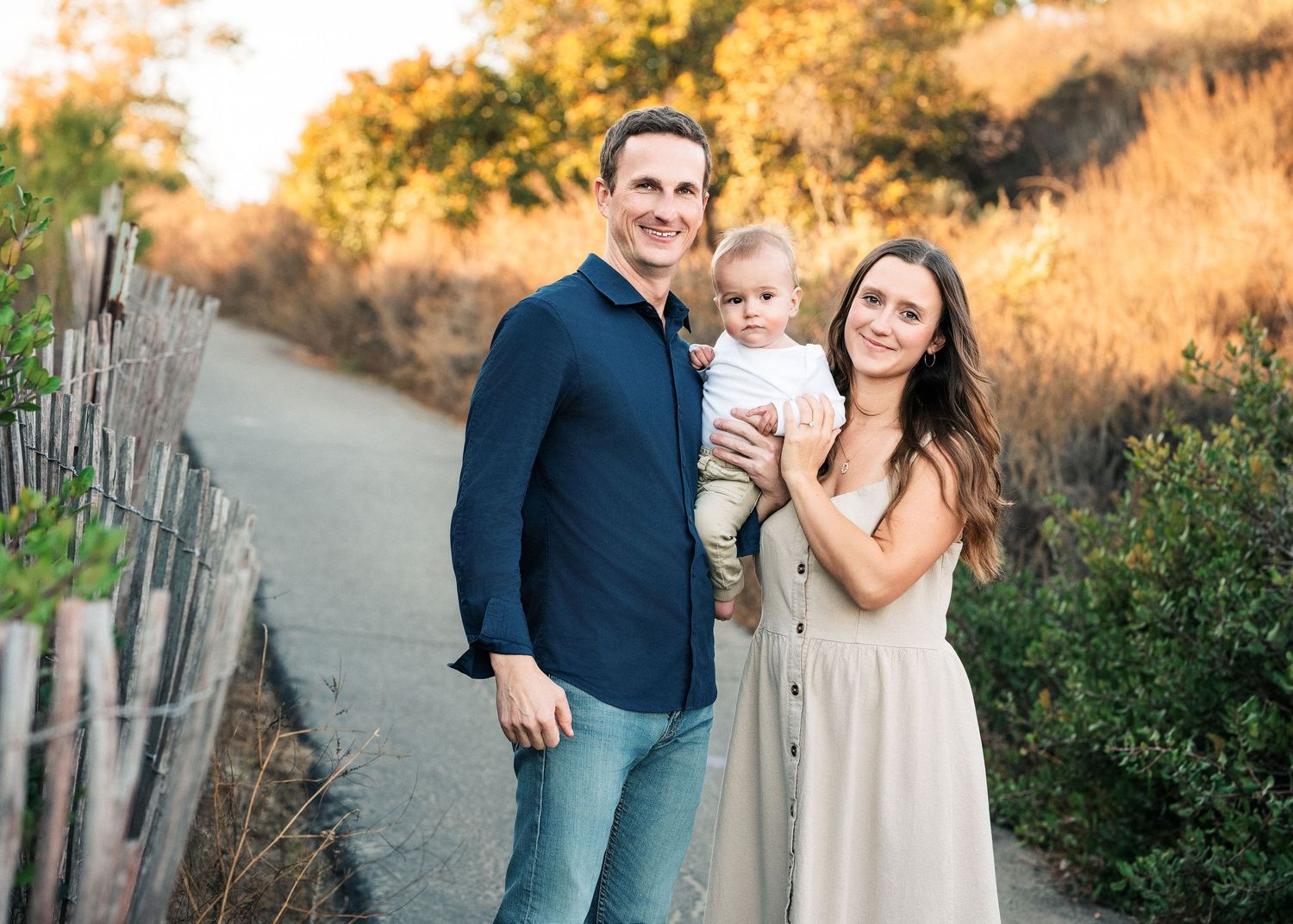 A family stands together on a peaceful path at sunset with golden light filtering through autumn foliage.