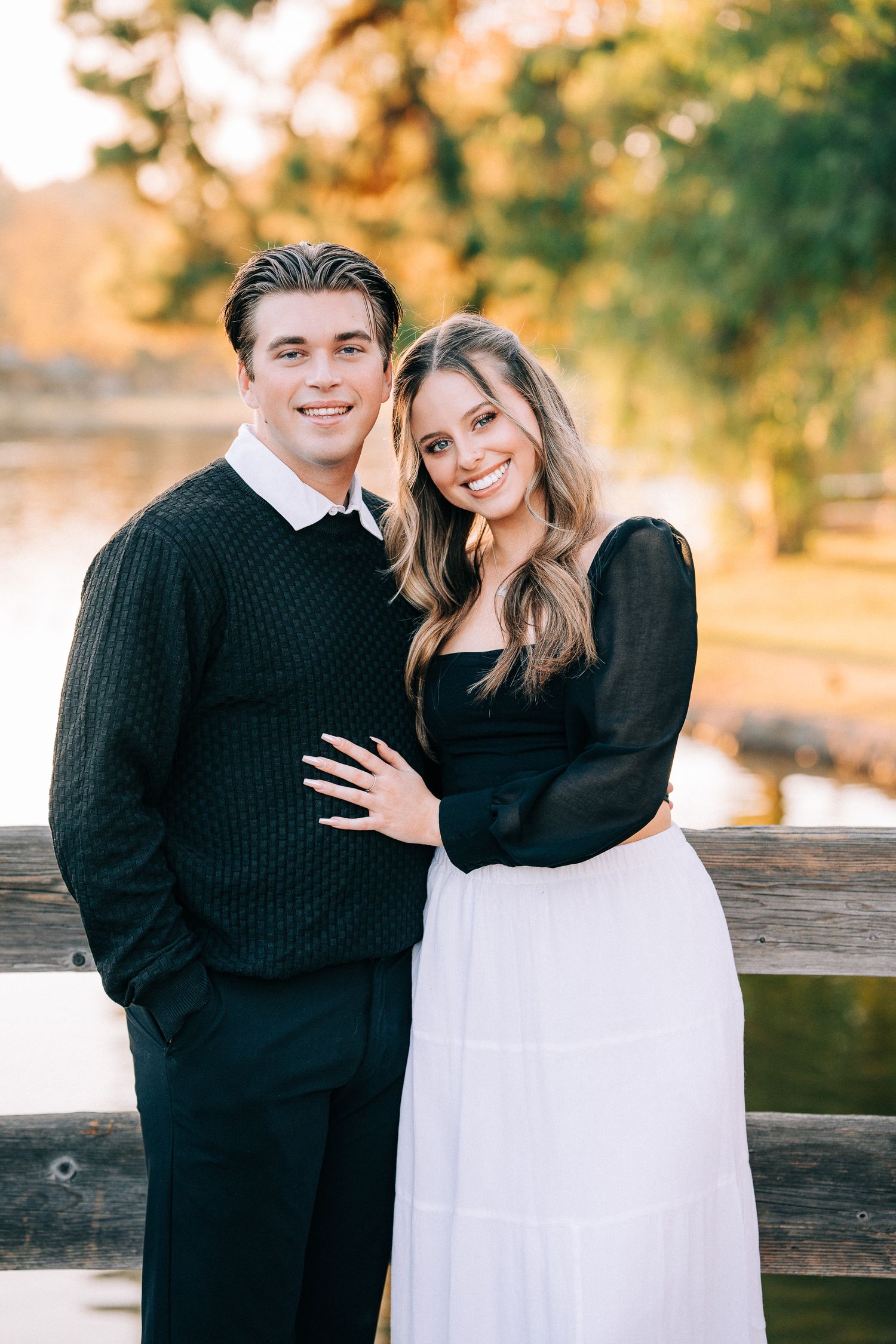 Romantic autumn engagement photos of a couple in black and white outfits embracing by a wooden fence.