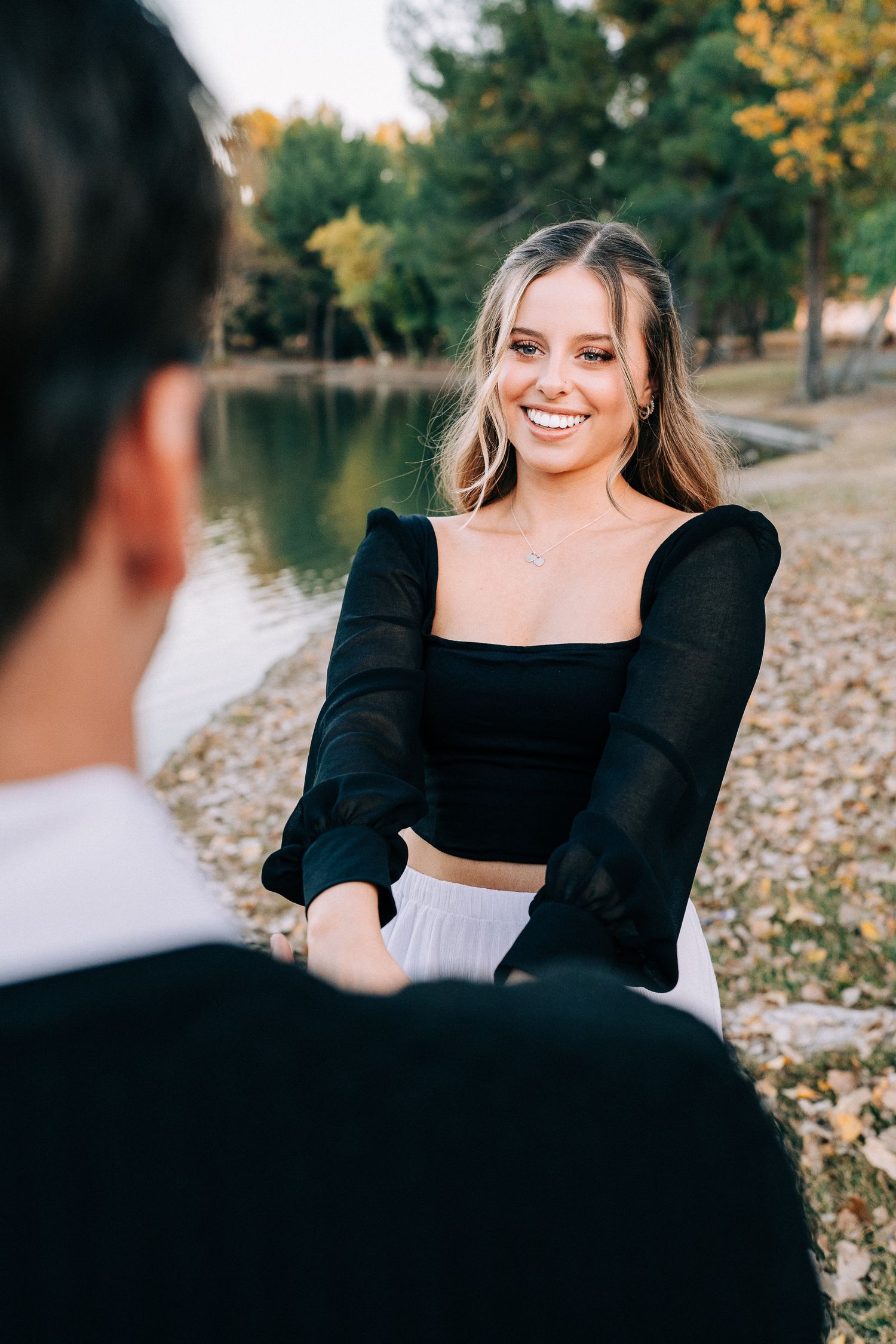 A joyful outdoor portrait by a lake showing a person in a black top and white skirt.