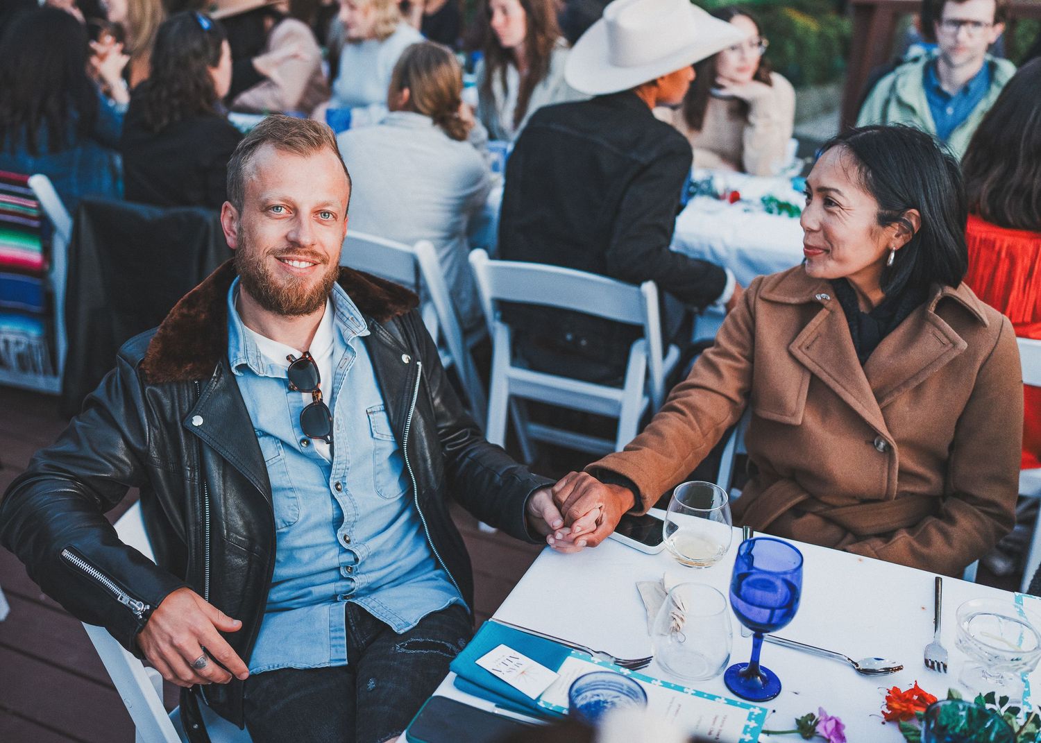 Guests seated at an outdoor table with blue wine glasses and decorative tablescapes.