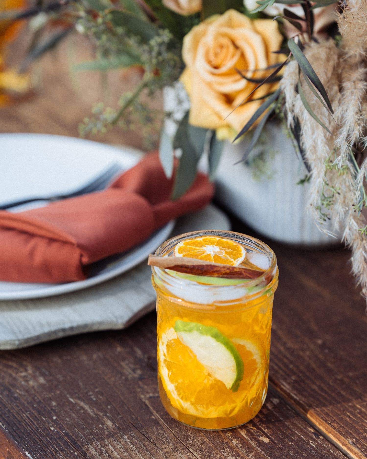 A refreshing citrus cocktail with orange slices garnished with a peach rose and linen napkins on a wooden table.