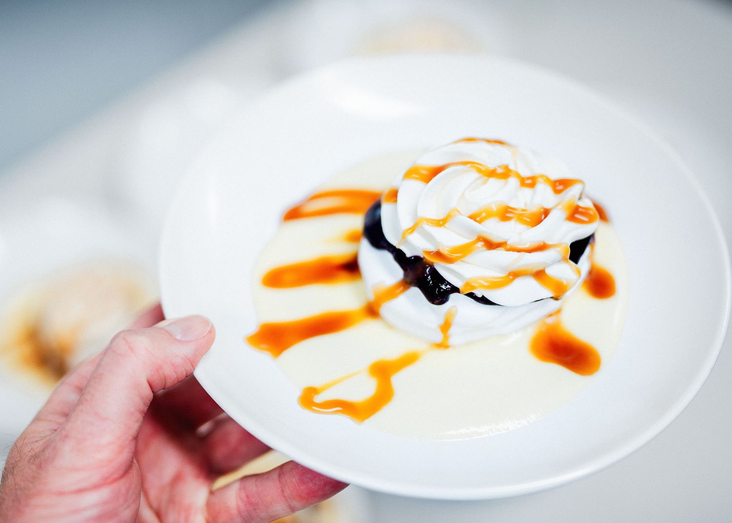 White dessert plate with caramel drizzle and whipped cream garnish held against bright background.