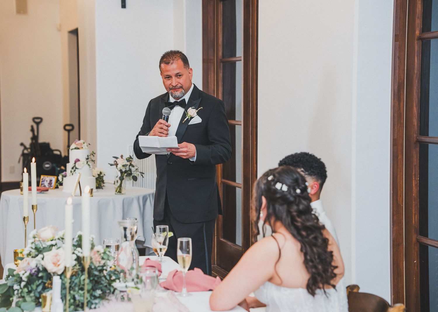 A decorated wedding reception table with white flowers and candlesticks in an elegant dining room setting.