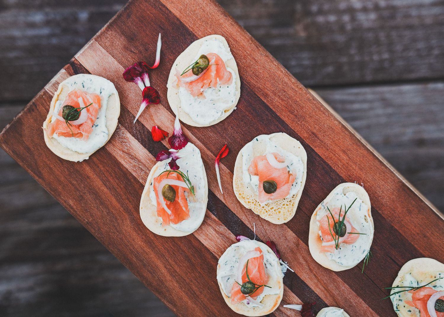 Small plates of smoked salmon, cream cheese, and dill canapes arranged on a rustic wooden serving board.