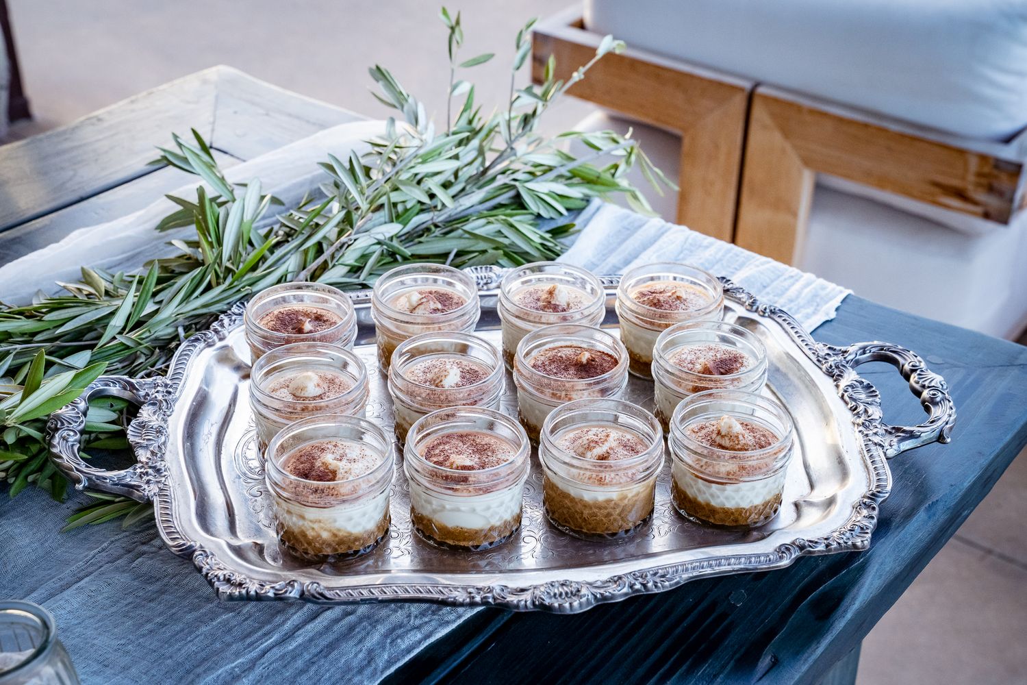 Individual dessert servings in glass jars arranged on an ornate silver serving tray with fresh herbs.