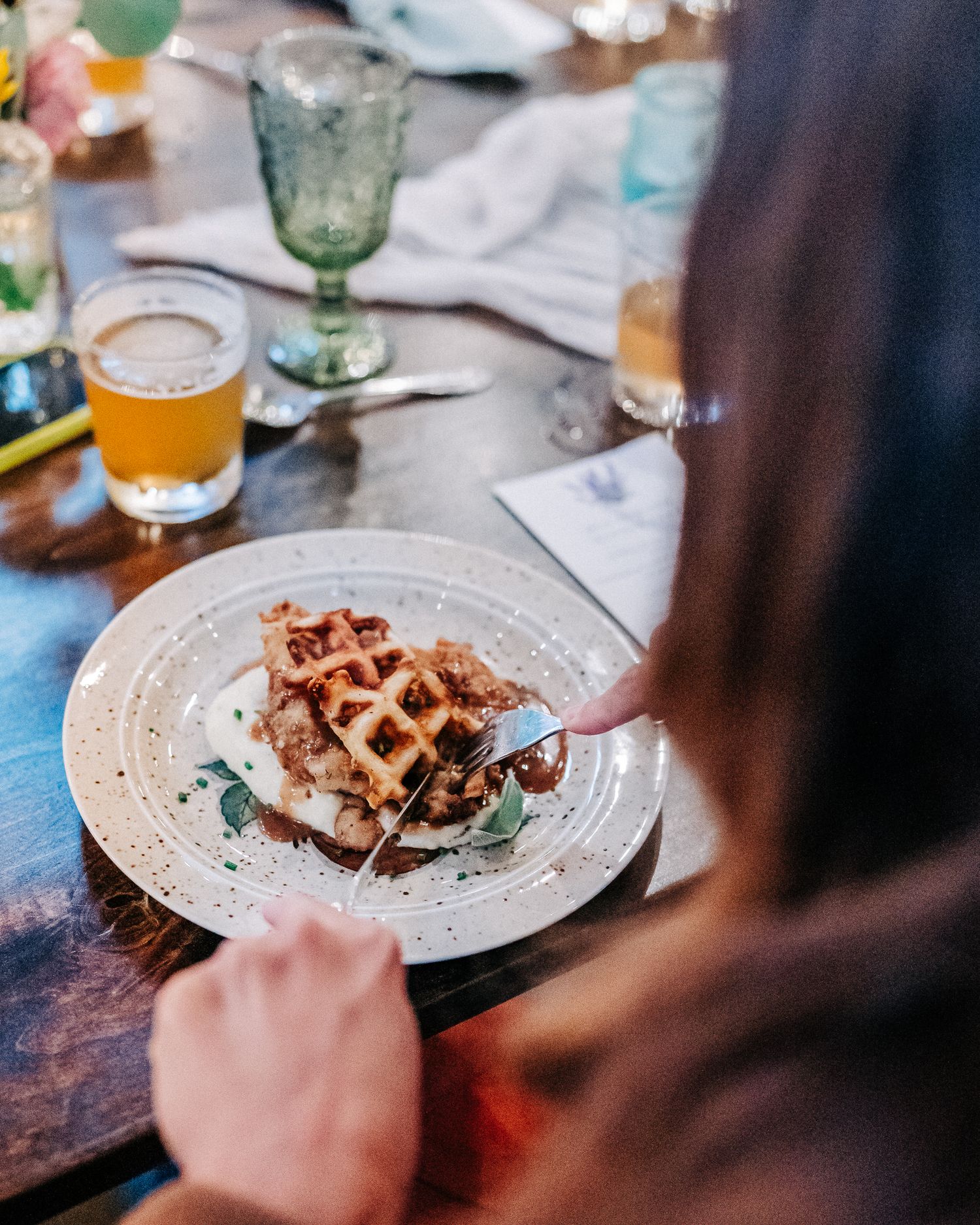 Homemade waffle with toppings served on a speckled plate next to a glass of beer on rustic wooden table.