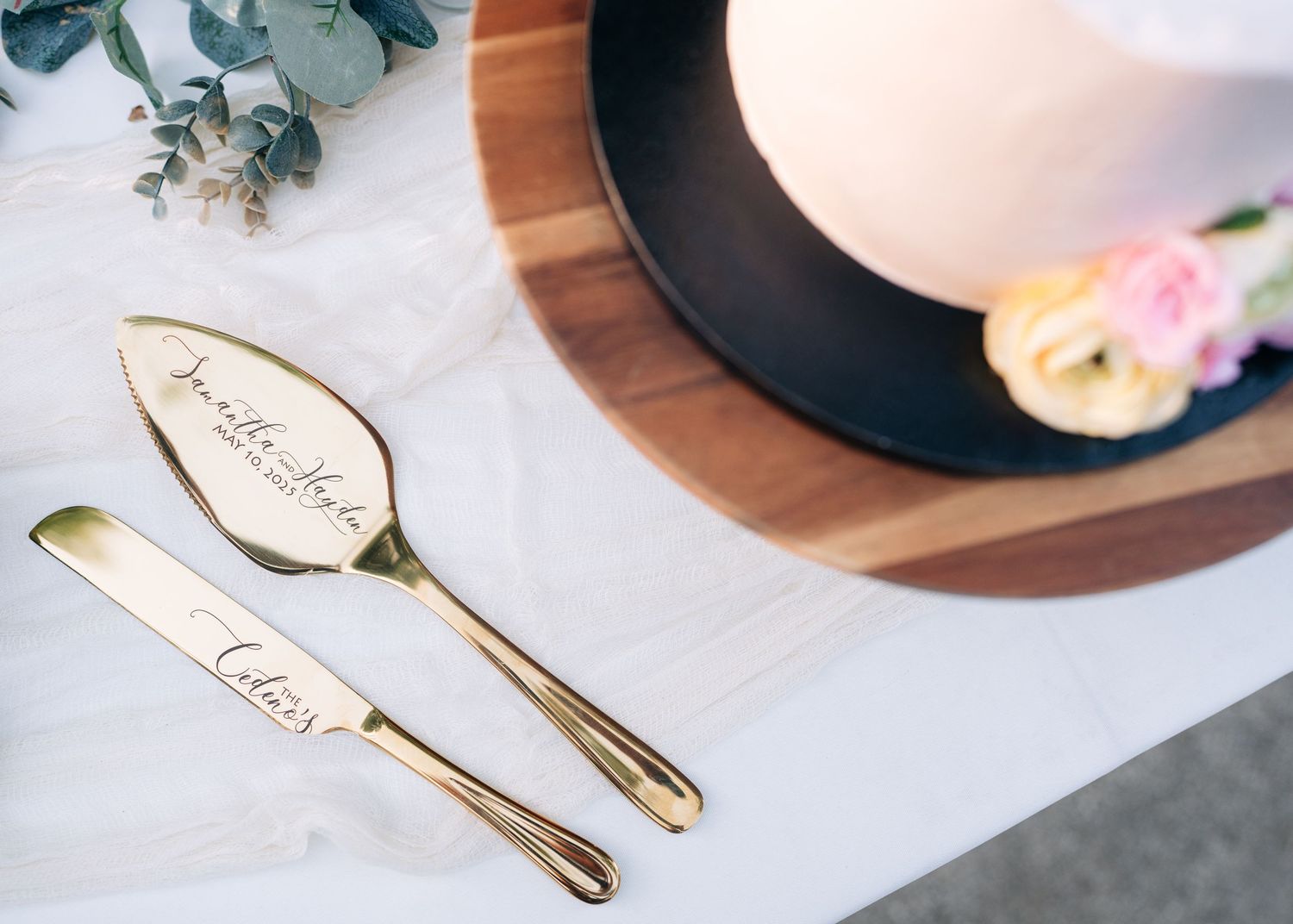Gold serving utensils and eucalyptus leaves arranged on a light colored surface for an elegant table setting.