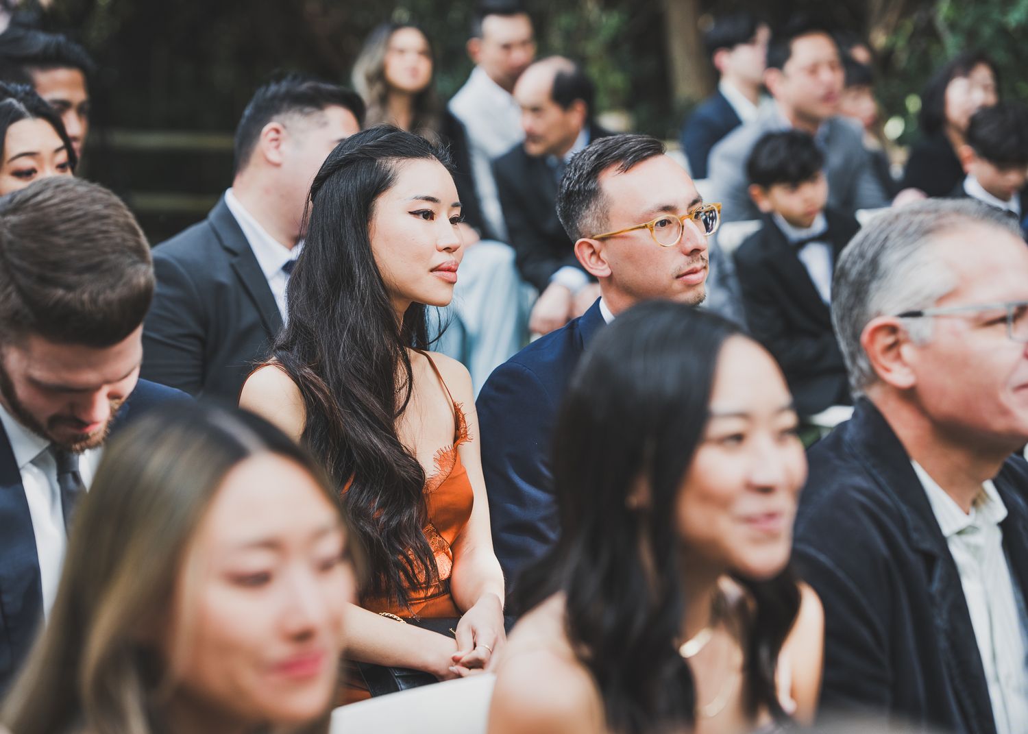 Wedding guests seated outdoors watching a ceremony with decorative floral arrangements.