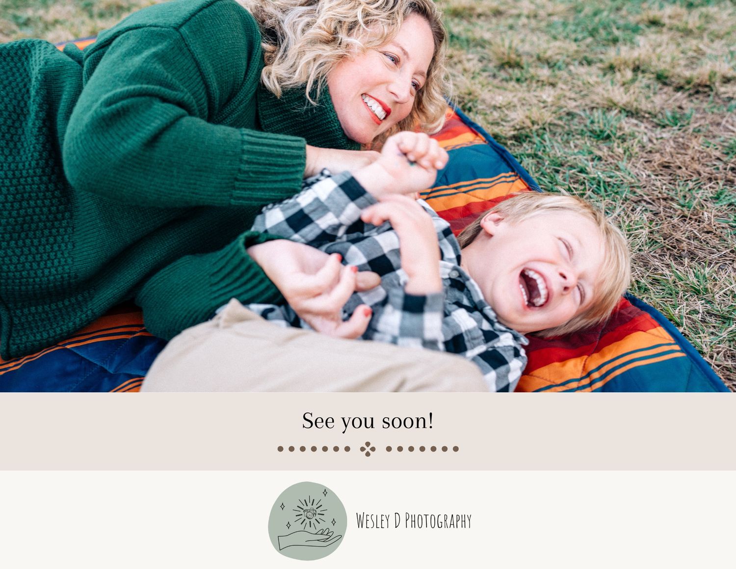 Two people laugh joyfully while laying on a colorful blanket outdoors on the grass.