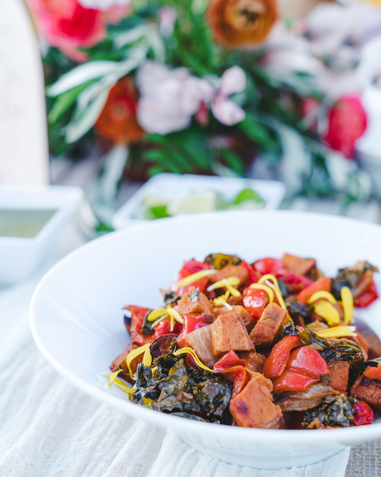 Colorful stir-fried dish with meat and vegetables served on a white plate with red tomatoes and dark leafy greens.