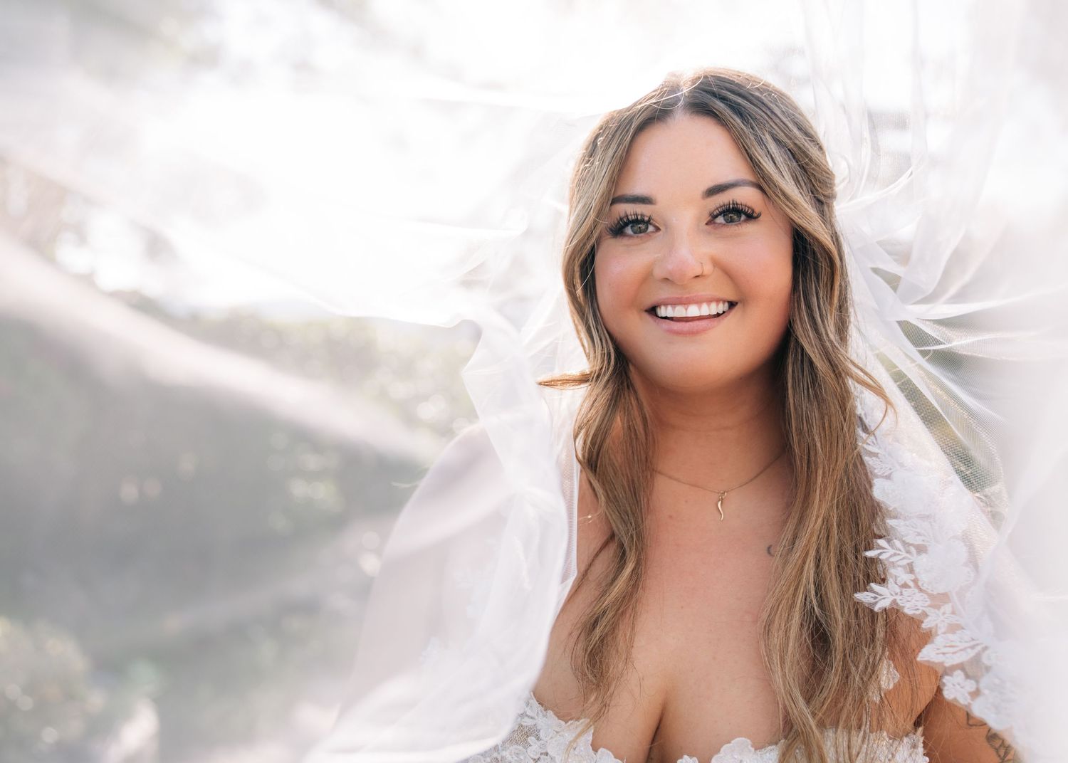 A joyful portrait of someone in a white dress with long wavy hair against a bright, dreamy background.