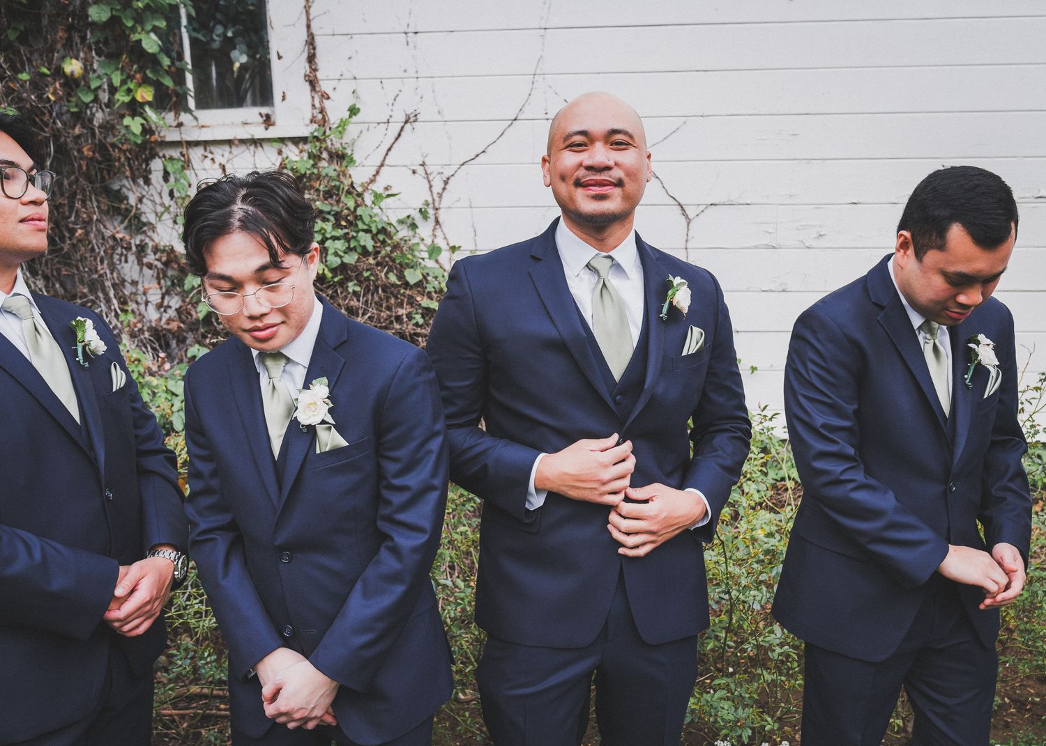 Groomsmen in navy suits sharing candid laughing moments outdoors.