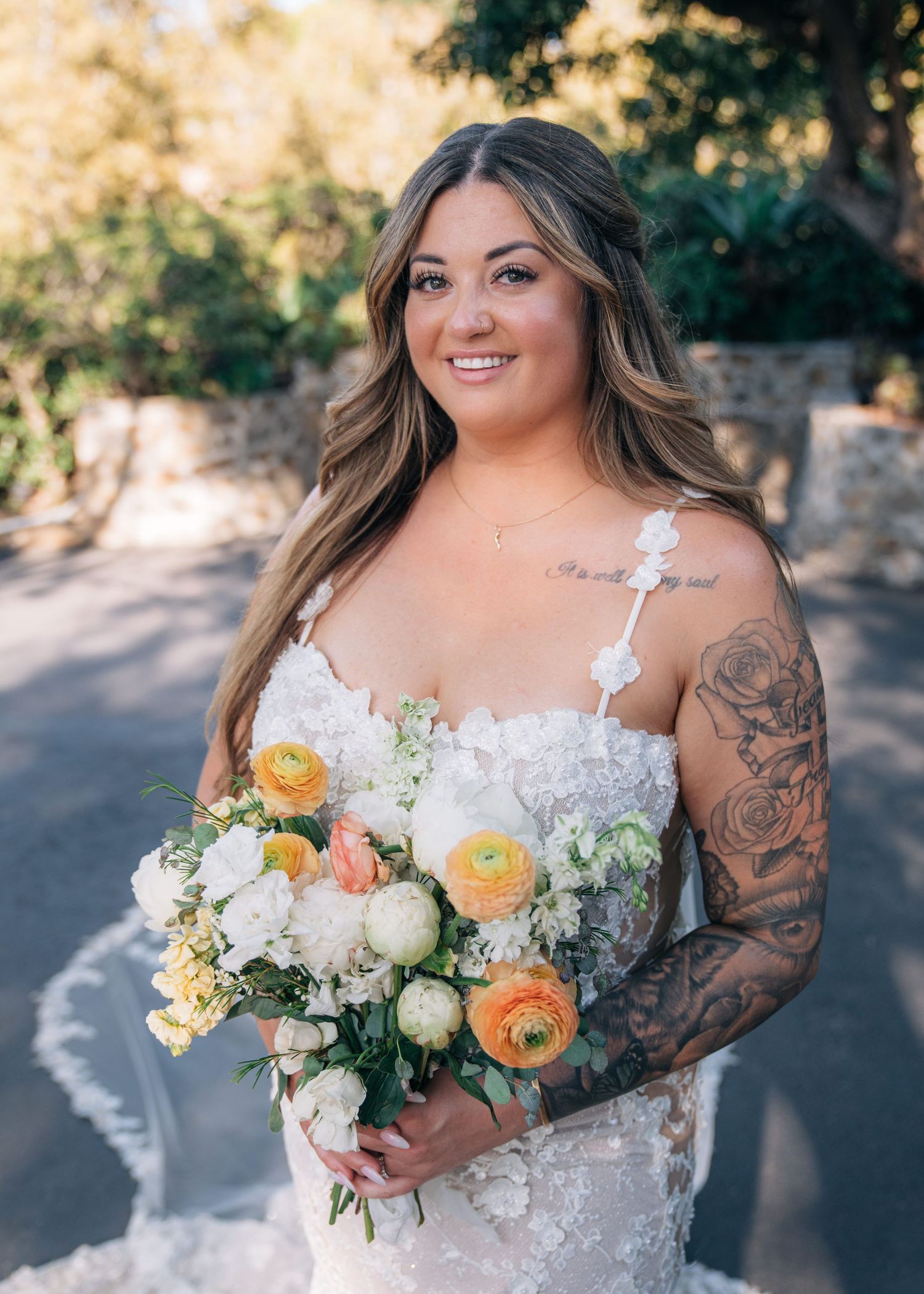 A bridal bouquet featuring white and peach-colored blooms with greenery against an outdoor forest backdrop.