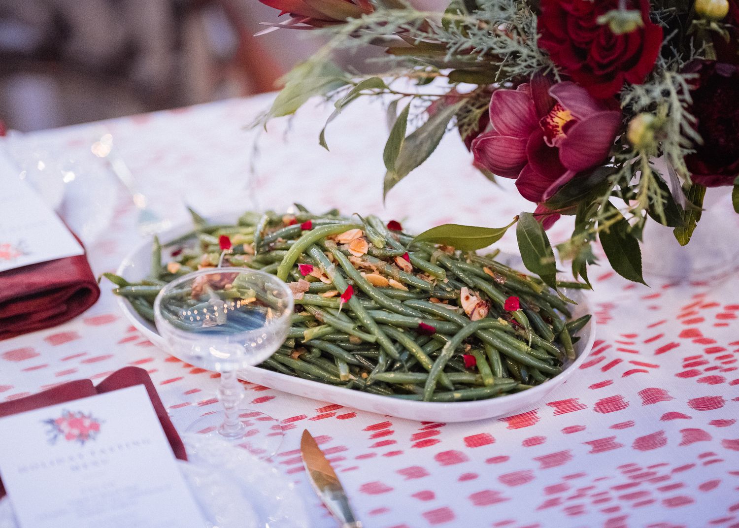 Green beans with red peppers served on white plate with floral decorations and red napkins.