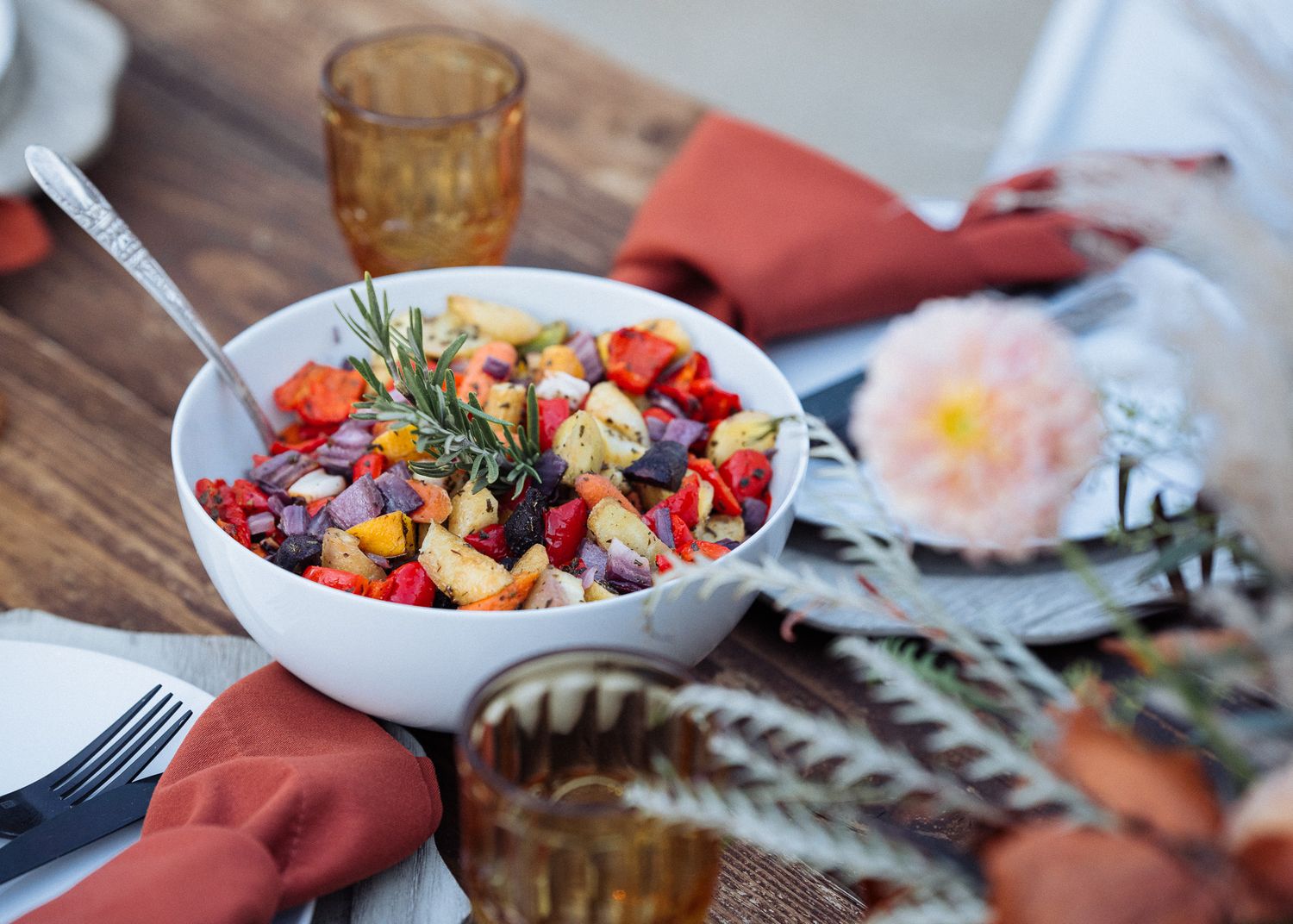 Fresh colorful salad bowl with mixed vegetables and herbs on rustic wooden table with table settings.