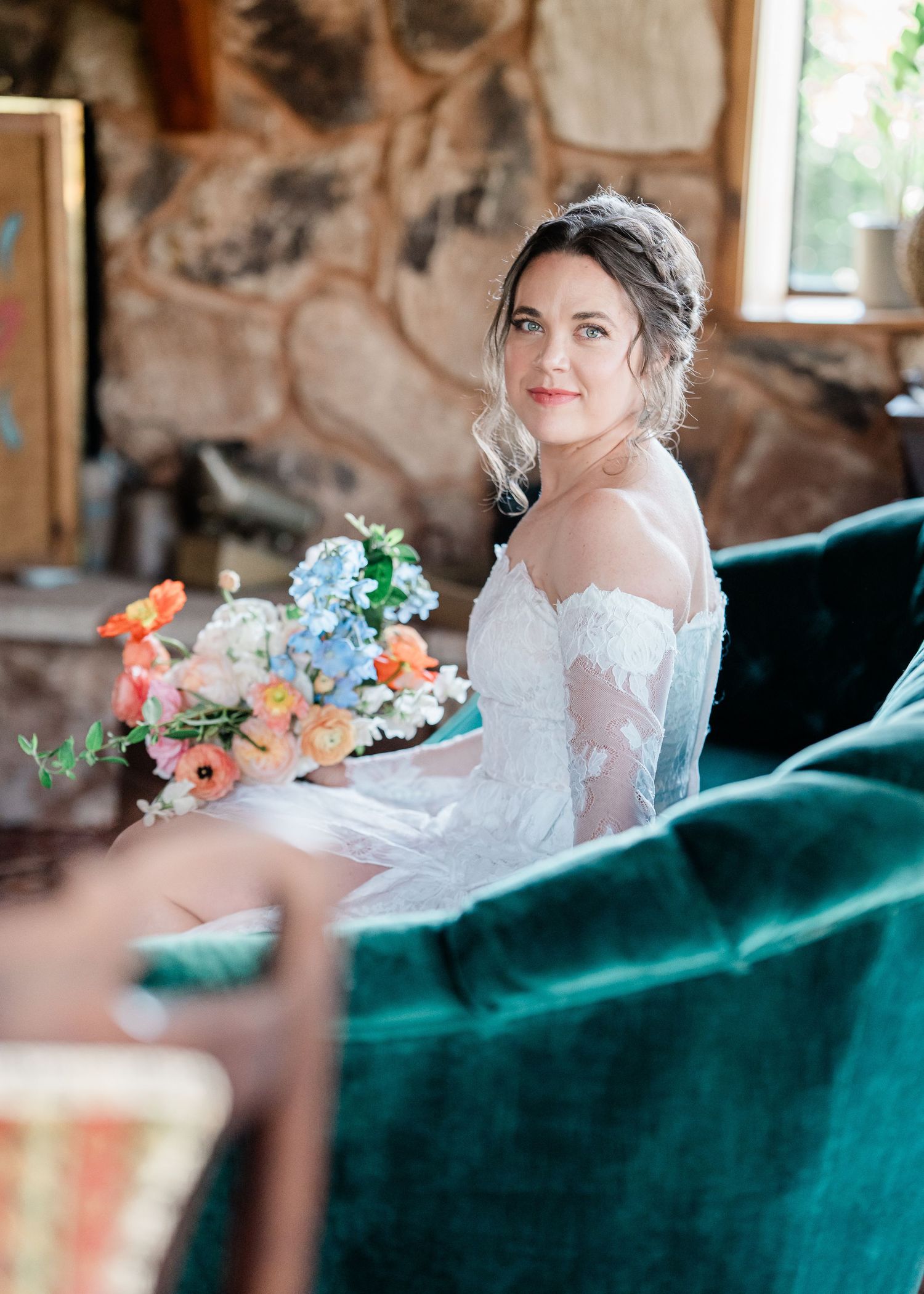 Elegant bridal portraits in lace gown with colorful bouquet against emerald velvet sofa.
