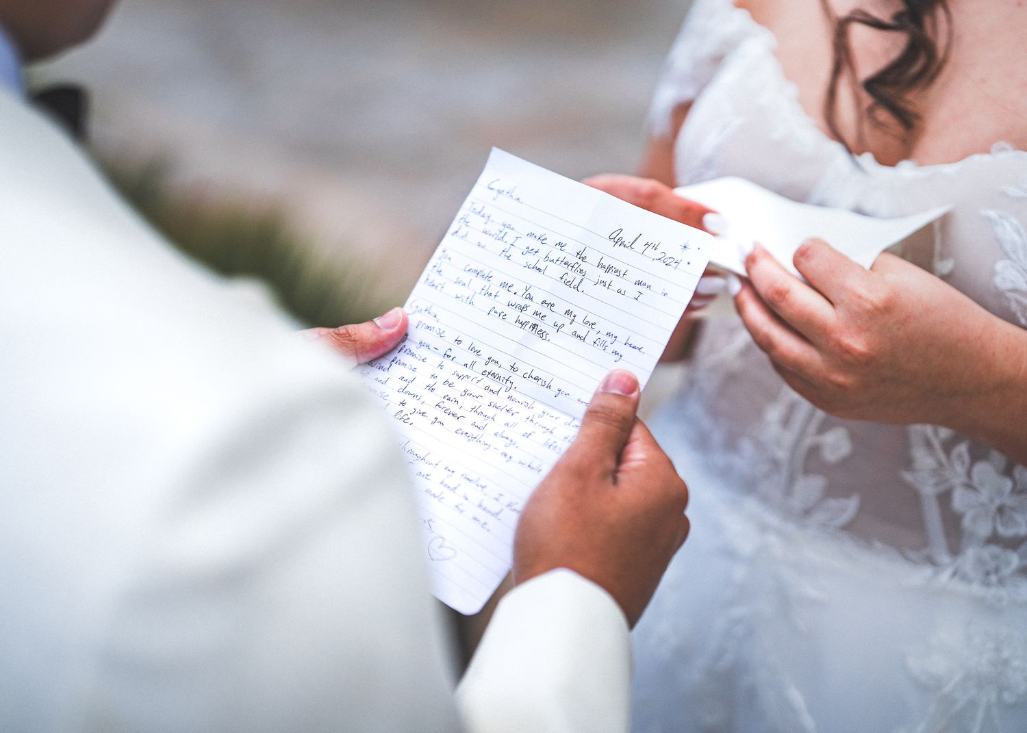 Close-up of hands holding handwritten wedding vows on white paper against a light background.