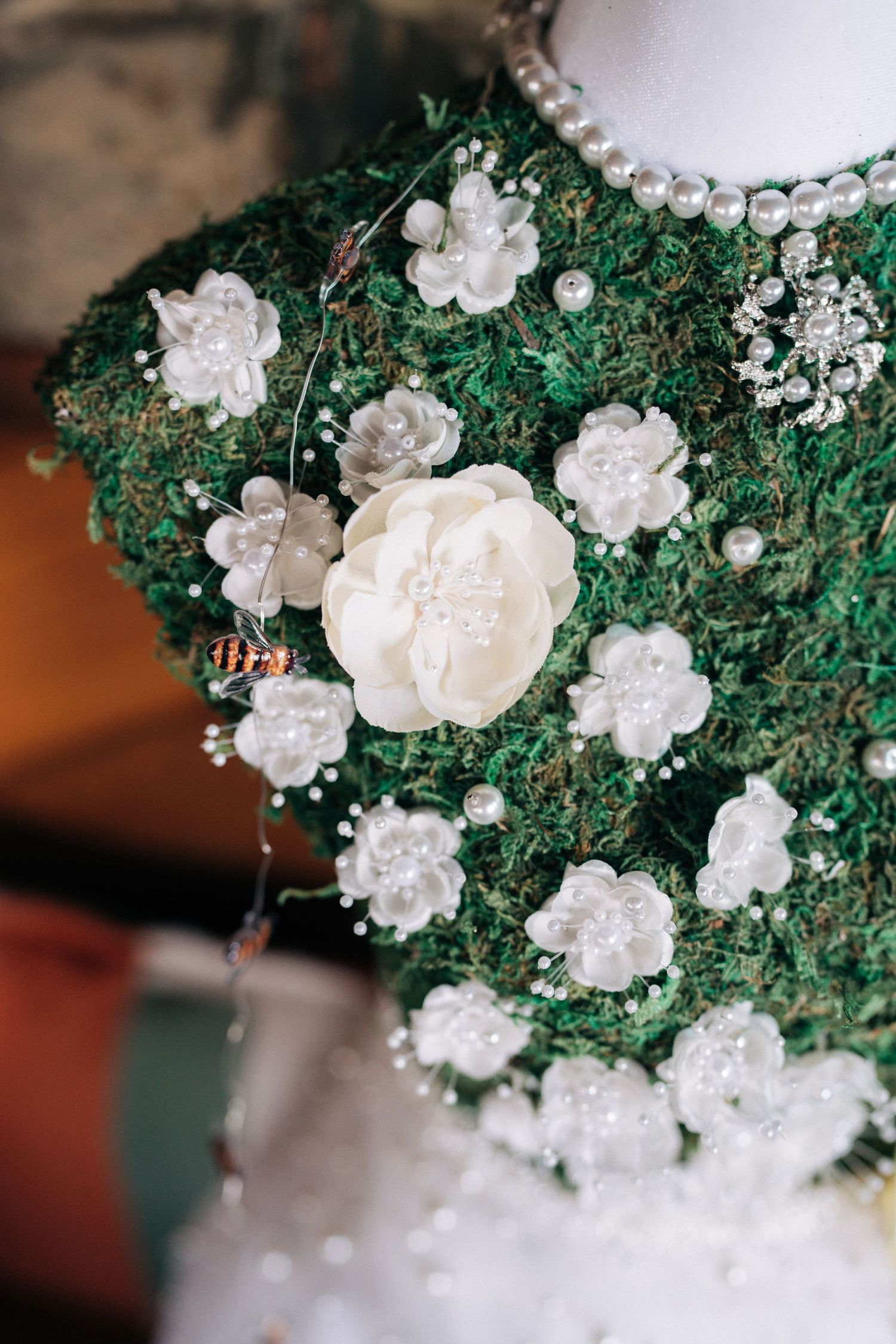 Delicate white flowers and pearls arranged on green moss wedding decor.