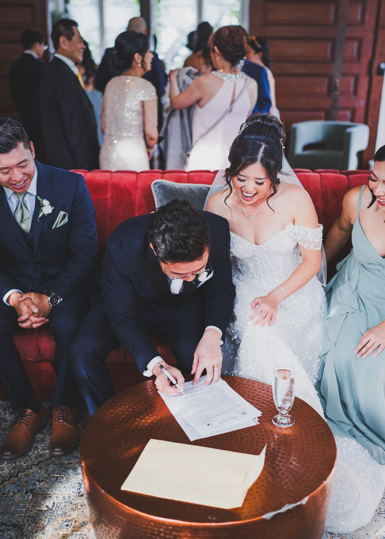 Wedding party signing documents at wooden table during ceremony.
