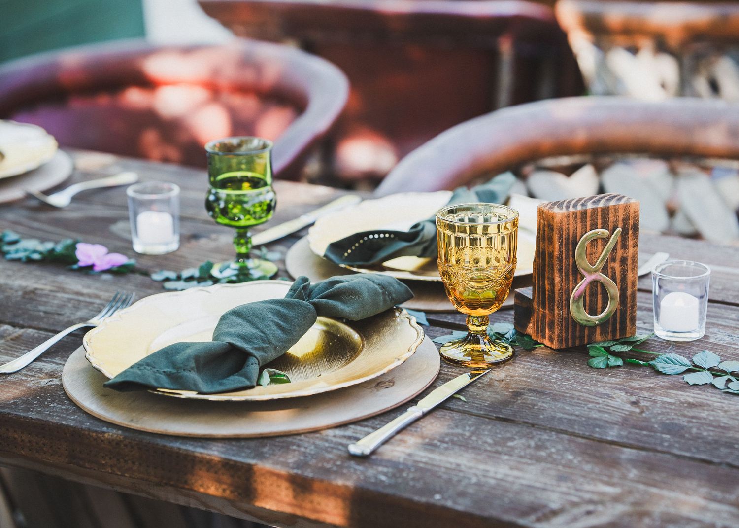 An elegant table setting with teal napkins, gold glasses and rustic details for a wedding reception.