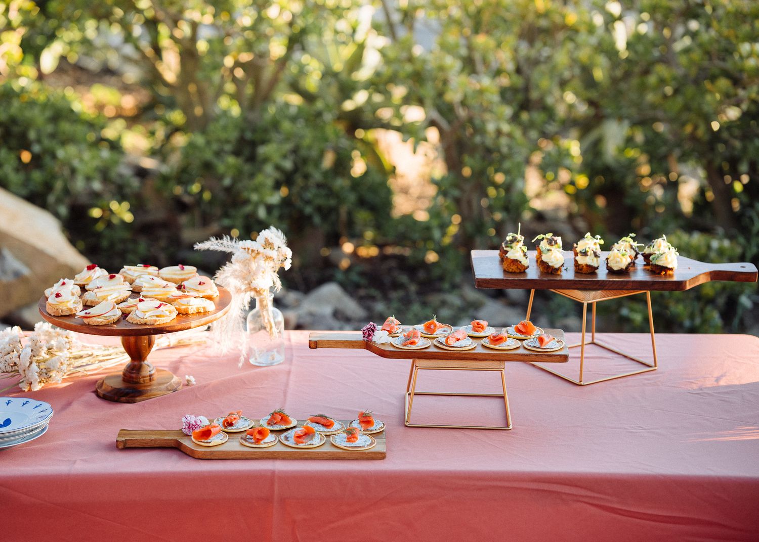 Elegant dessert table with tiered displays of cupcakes and appetizers on a coral tablecloth.