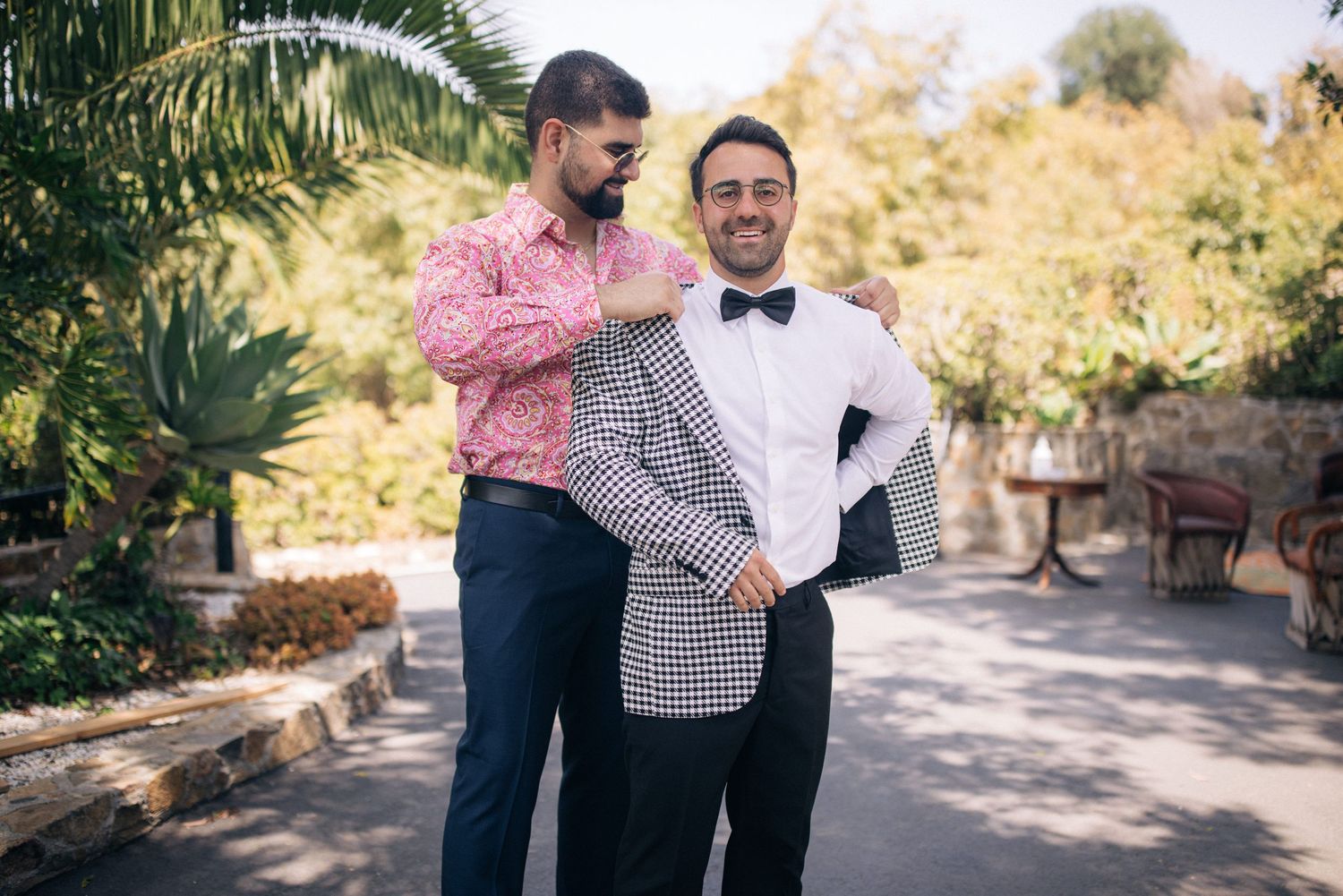 Two people in formal attire getting ready for a special event in an outdoor garden setting.
