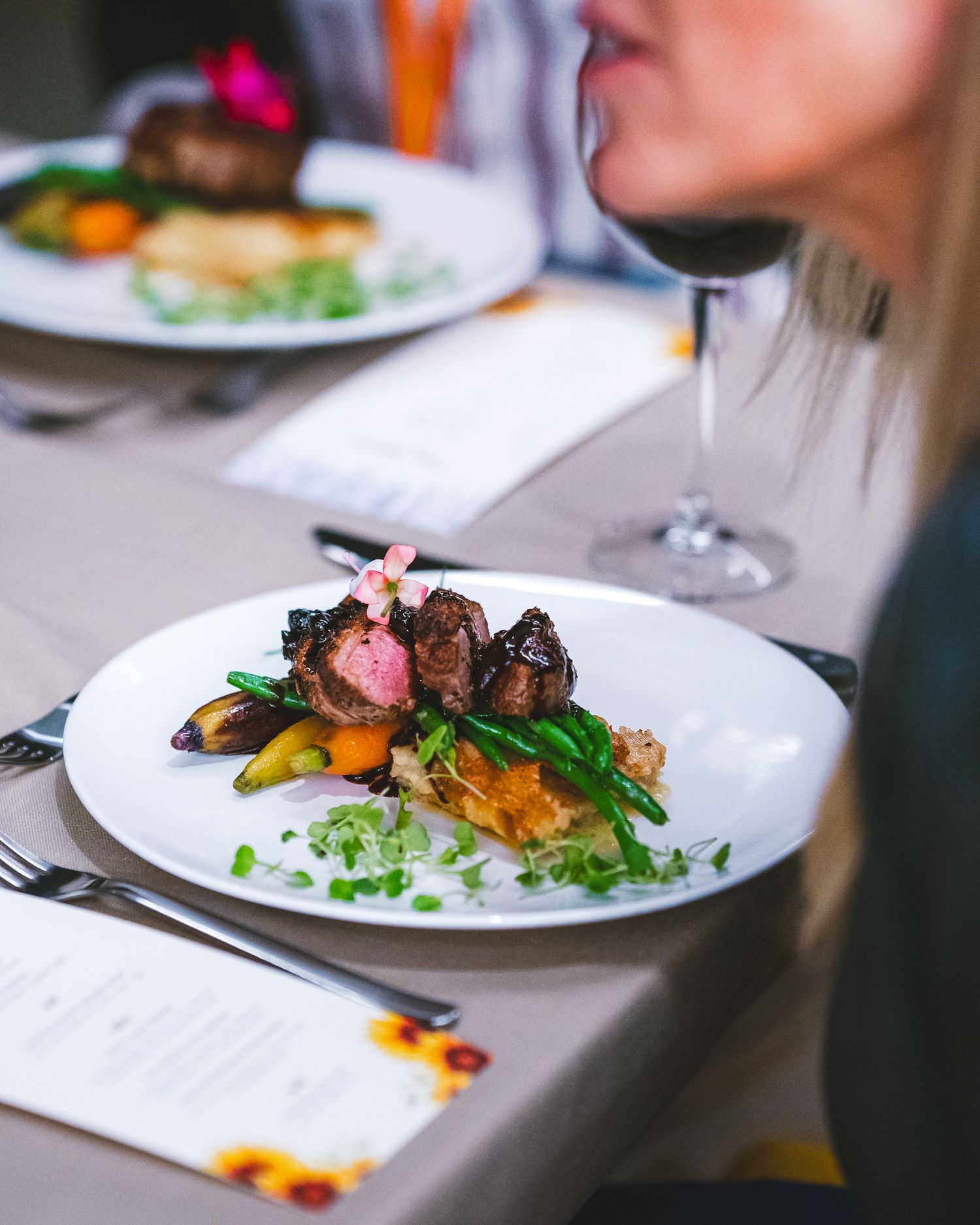 Elegantly plated medium-rare steak with colorful vegetables and microgreens served on a white plate with wine glass.