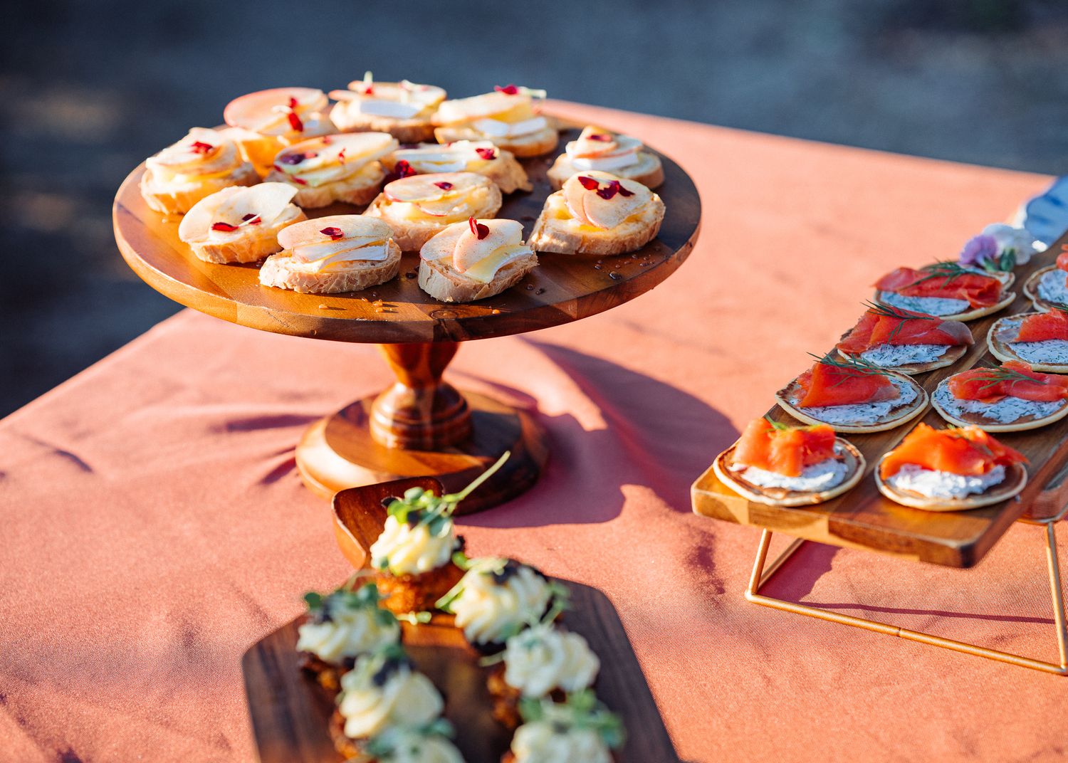 Elegant dessert display featuring pastries on copper cake stands with succulents on a coral tablecloth.