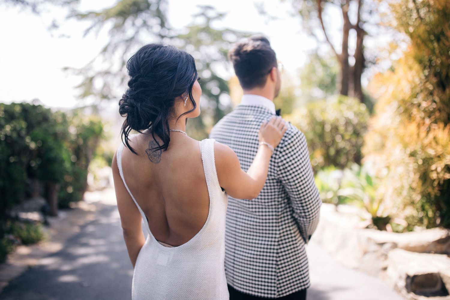 Elegant couple in formal attire walking along garden pathway.