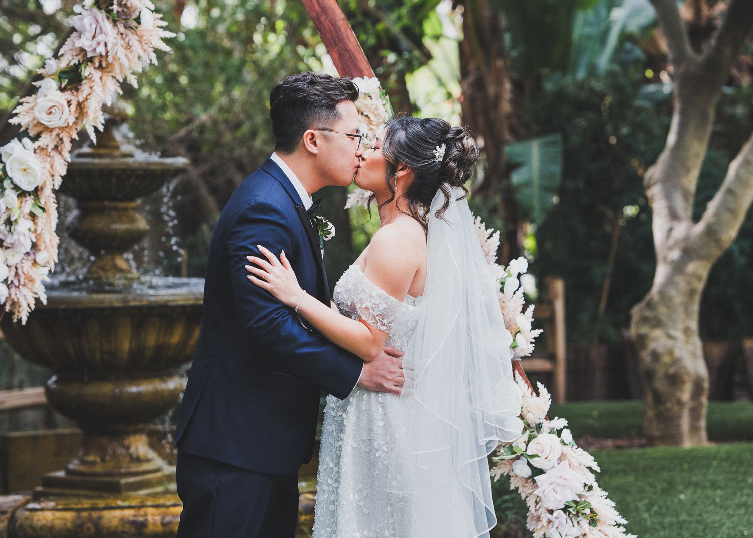 Romantic wedding moment by ornate fountain with floral decorations.