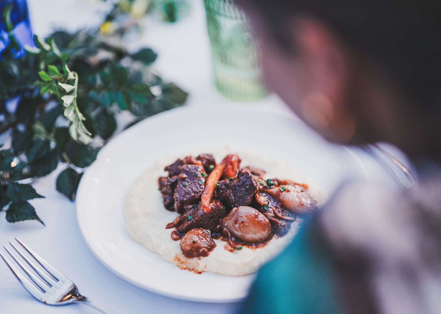 A plate of grilled octopus with sauce served at a restaurant table with greenery in the background.