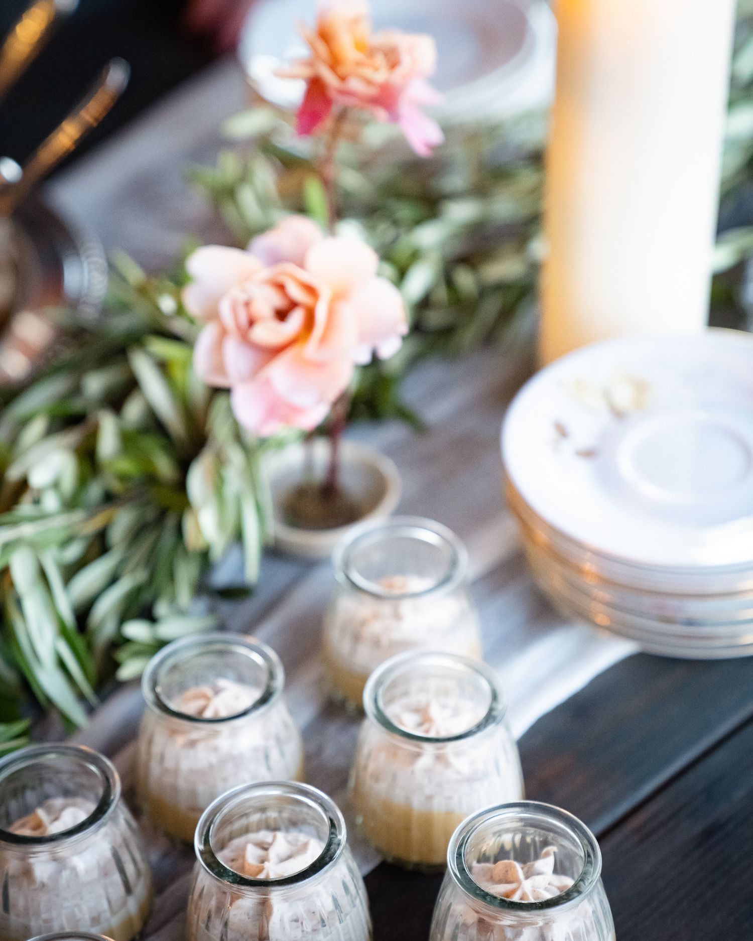 Glass jars of drinks with roses and greenery decorating an elegant table setting.