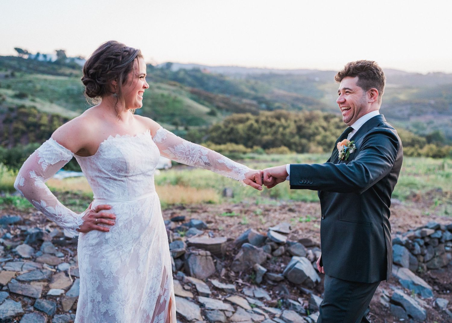 A candid moment between newlyweds laughing together on rocky terrain with mountains behind them.