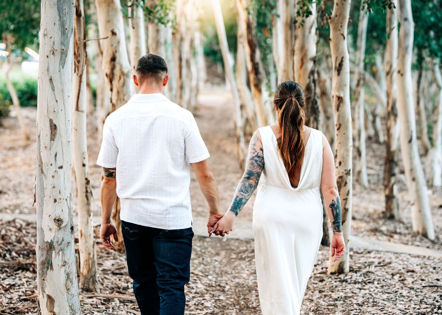 A couple walking hand in hand through a scenic path lined with white birch trees on a sunny day.