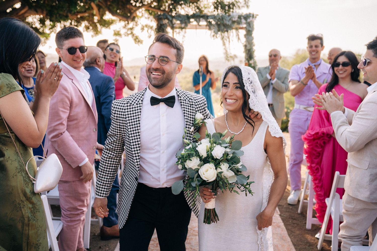 Newlyweds walking through a crowd of well-wishers at an outdoor garden celebration.